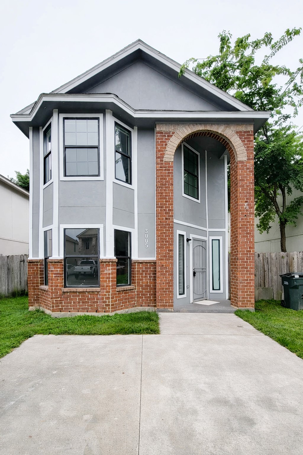 Charming two-story home featuring a striking combination of gray siding and brick accents, with a welcoming arched entry and large bay windows.