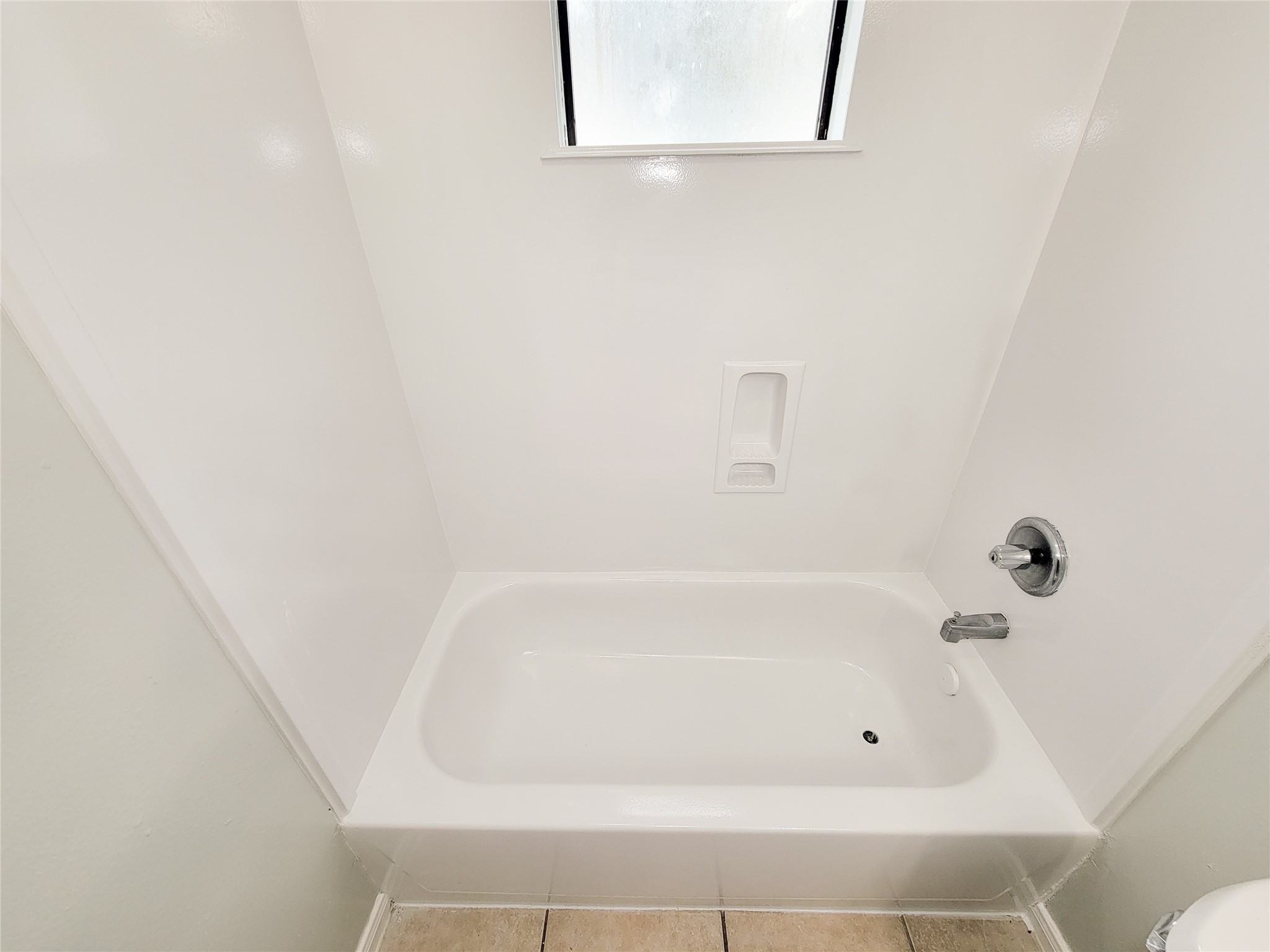 A pristine, white bathtub with modern fixtures, accompanied by a frosted window for natural light and privacy.