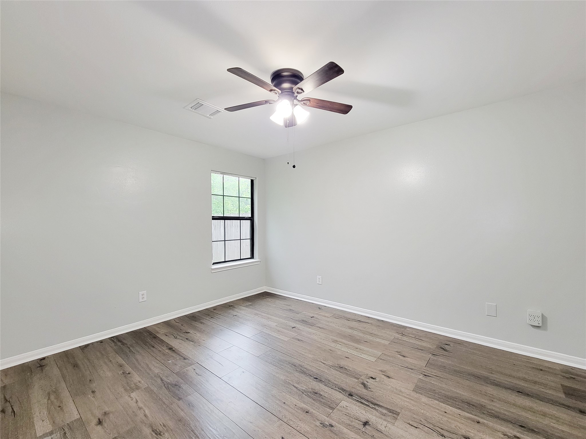 Spacious bedroom featuring elegant wood flooring, a modern ceiling fan, and abundant natural light from the large window.