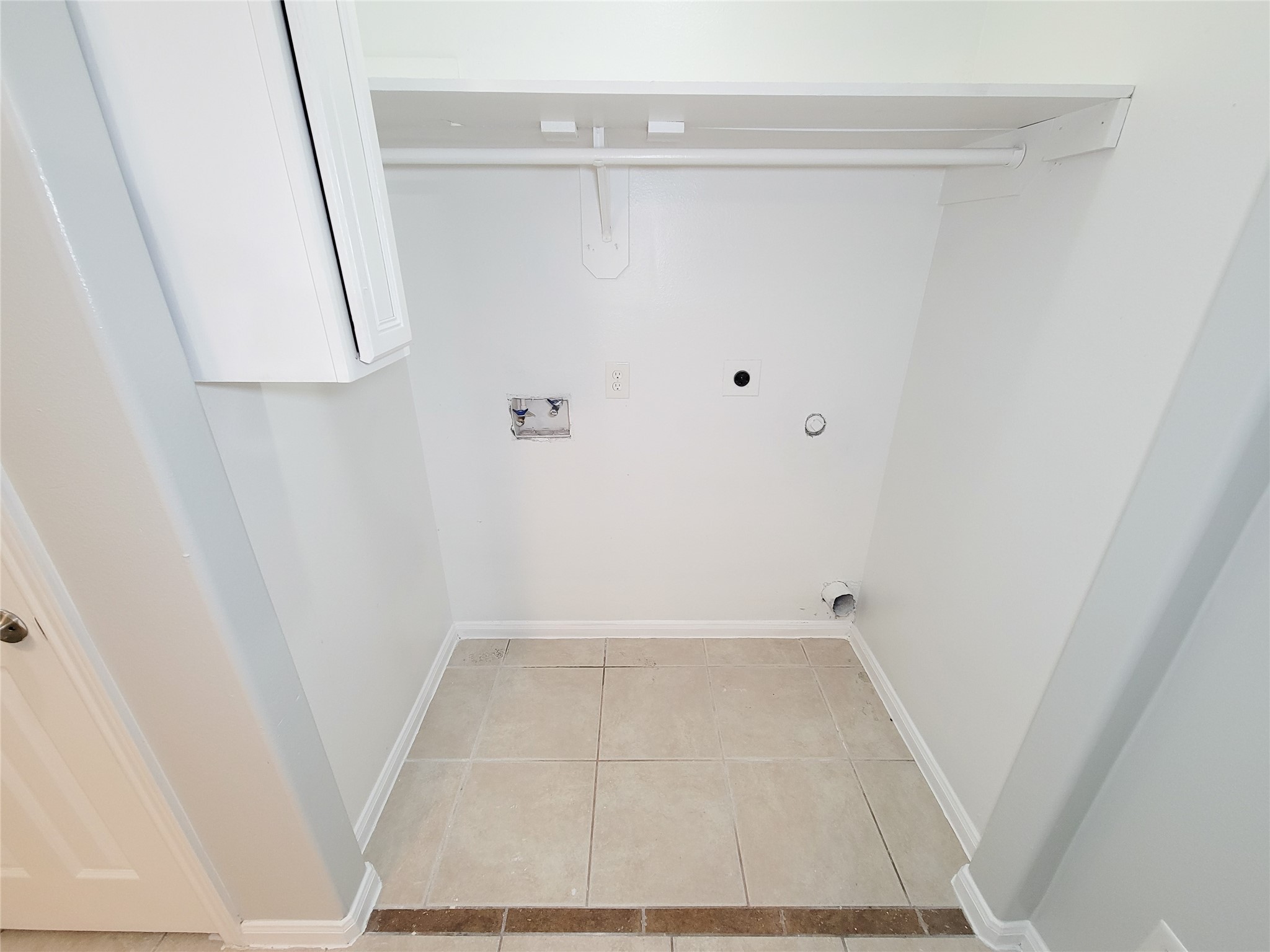 Spacious laundry area with hookups, featuring a convenient overhead shelf and tile flooring.