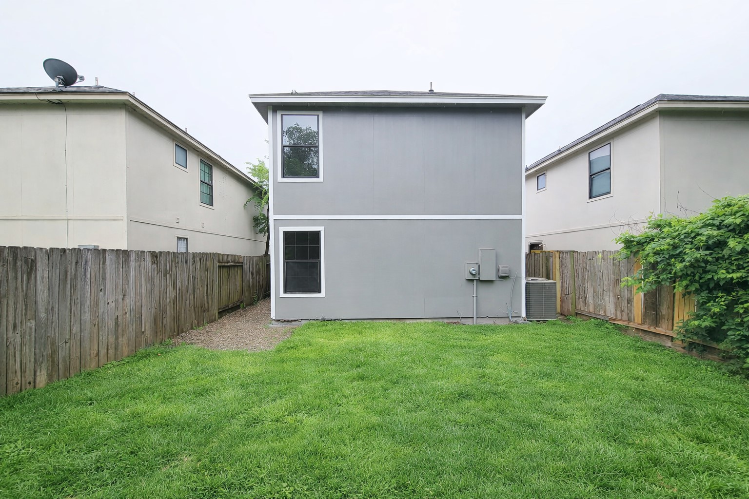 Charming two-story home with a neatly fenced backyard and lush green lawn, perfect for outdoor activities and entertaining.