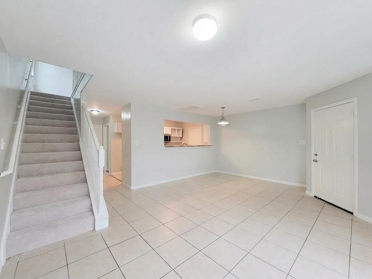 Bright and spacious living area with tiled flooring, a cozy dining nook, and easy access to the kitchen. A carpeted staircase leads to the upper level, creating a welcoming atmosphere.