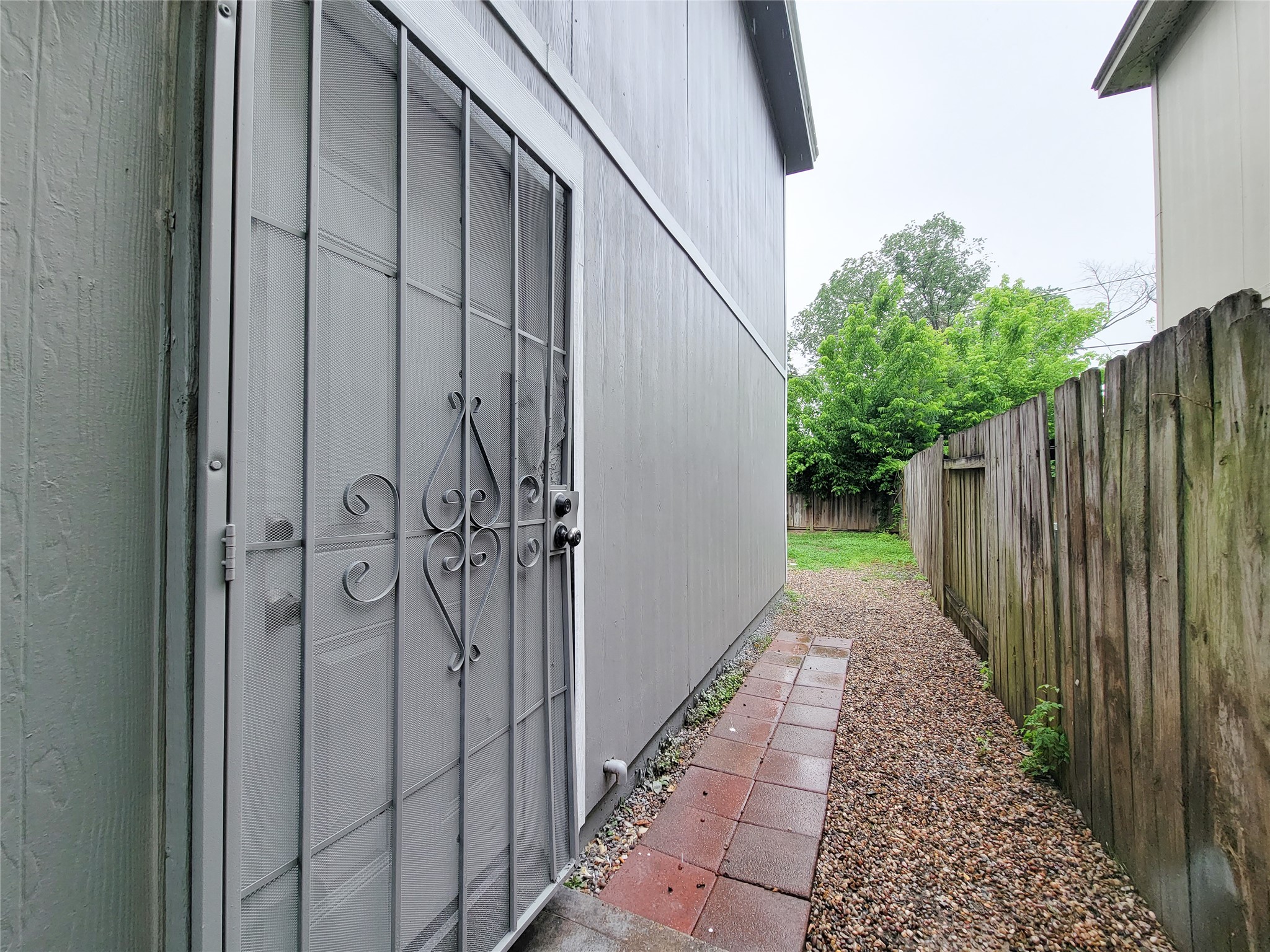Charming side yard with a secure wrought iron door, offering privacy and a pathway leading to a cozy backyard space.