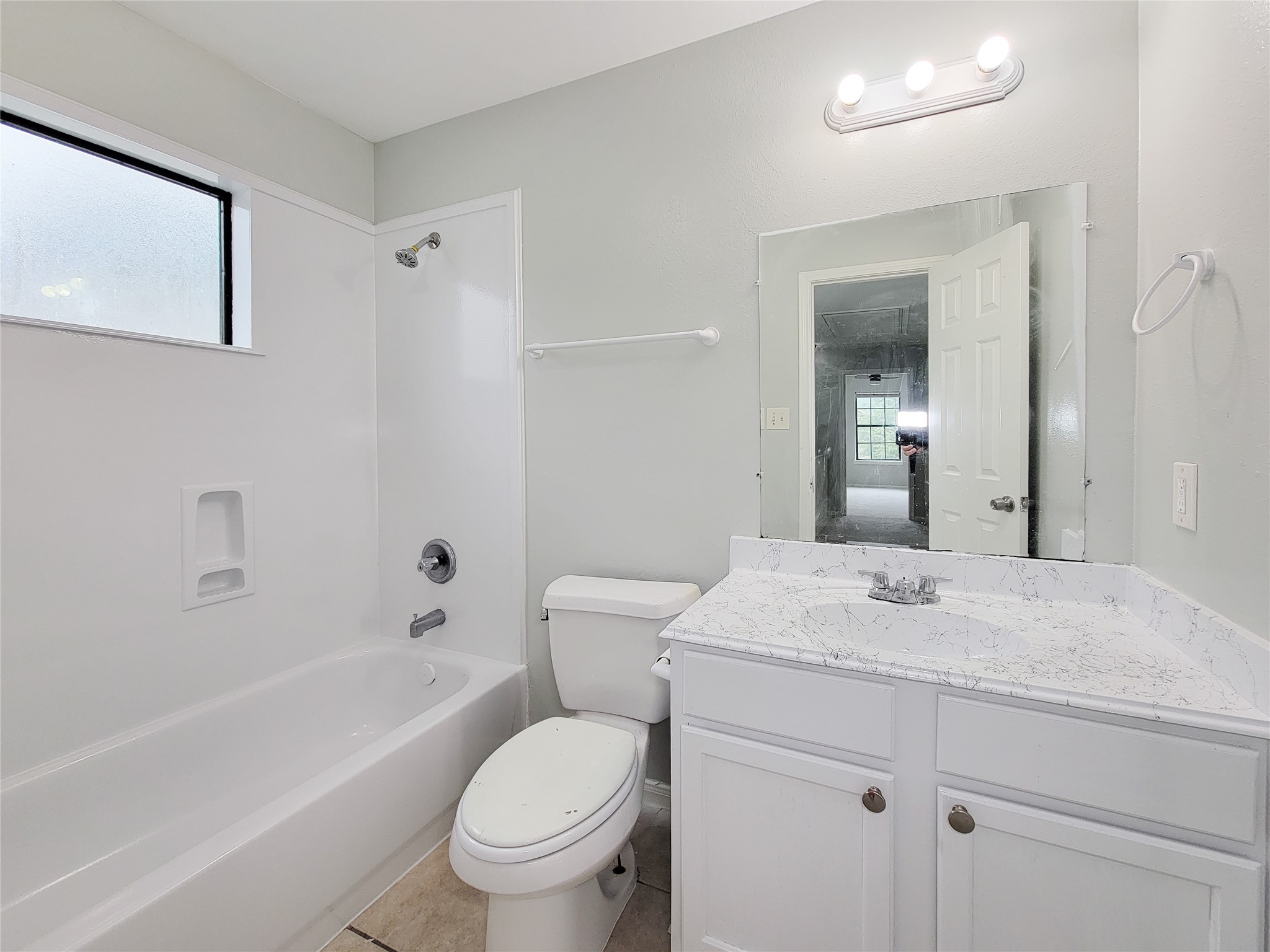 Bright and modern bathroom featuring a sleek vanity with a marble countertop, a full bathtub, and ample natural light from the frosted window.