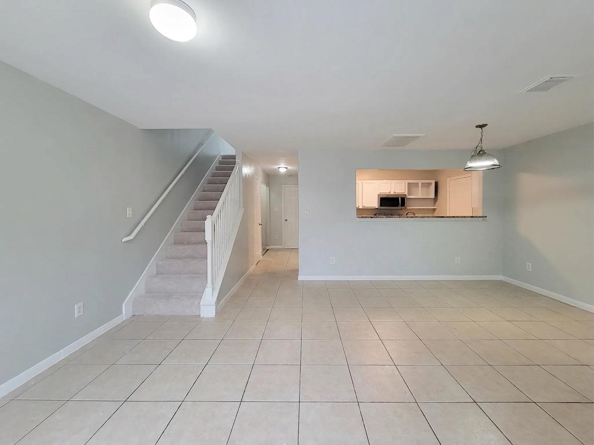 Spacious open-plan living area with tiled flooring, neutral walls, and a view into the modern kitchen. A staircase leads to the upper level, enhancing the home's layout.