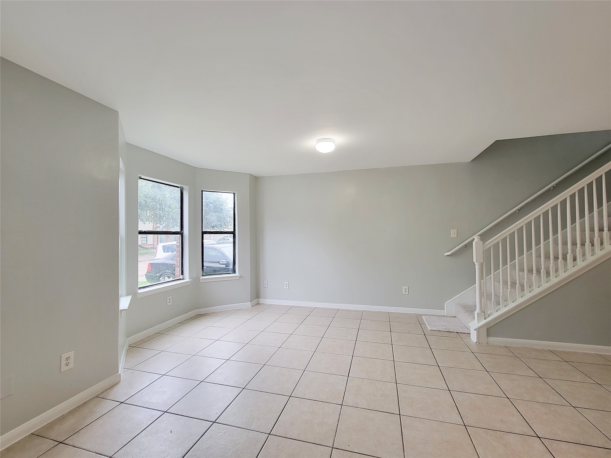 Spacious living area with abundant natural light, featuring a charming bay window and easy-to-maintain tile flooring, complemented by a staircase leading to the upper level.