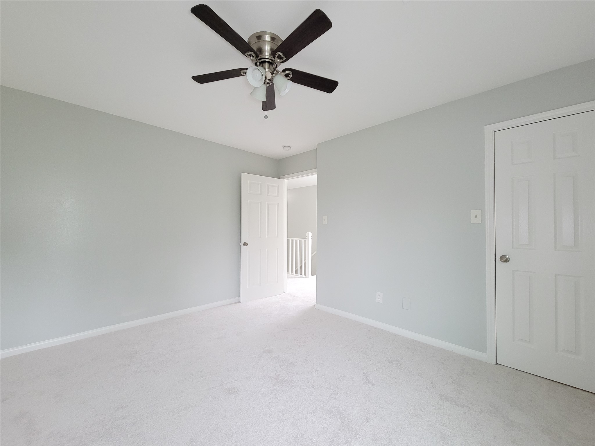 Bright and airy bedroom featuring soft gray walls, plush carpet, and a modern ceiling fan for comfort.