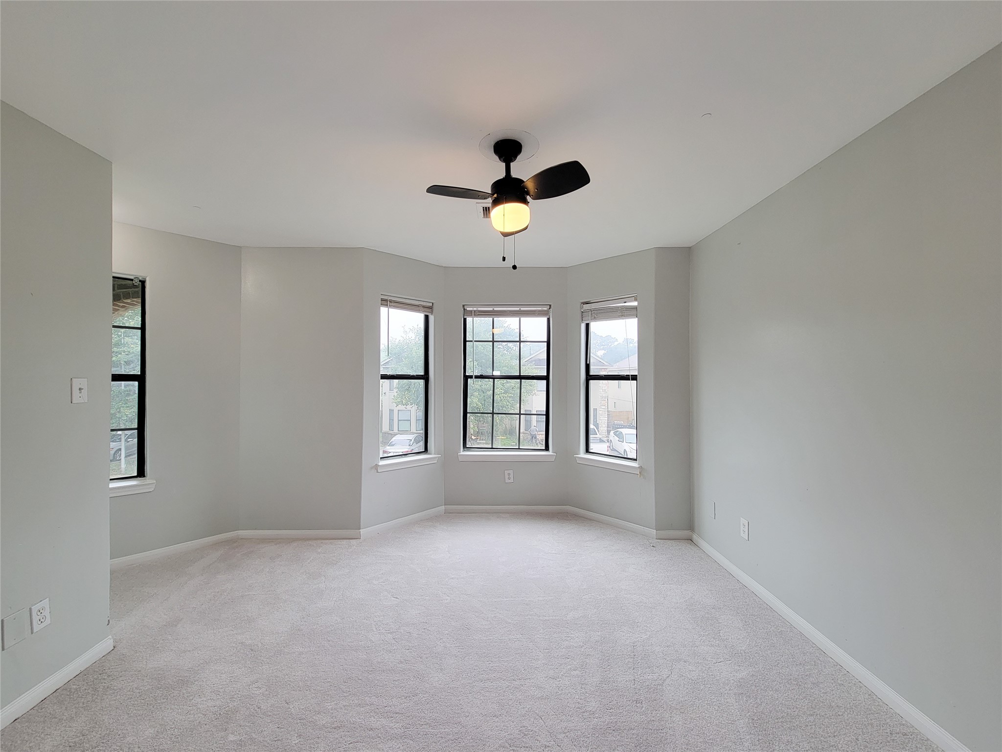 Bright and spacious room with a stylish ceiling fan, neutral walls, and abundant natural light pouring through multiple large windows.