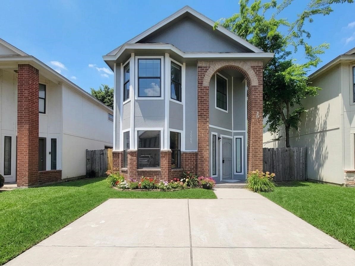Charming two-story home with elegant brick accents, lush green lawn, and vibrant flowers framing the entrance for a welcoming curb appeal.