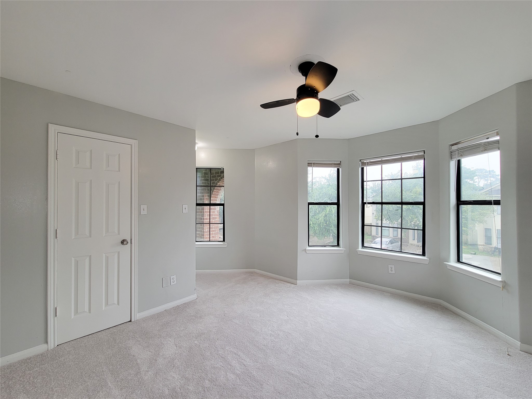 Bright and spacious bedroom featuring large windows, a modern ceiling fan, and soft carpeting, creating a comfortable and inviting atmosphere.