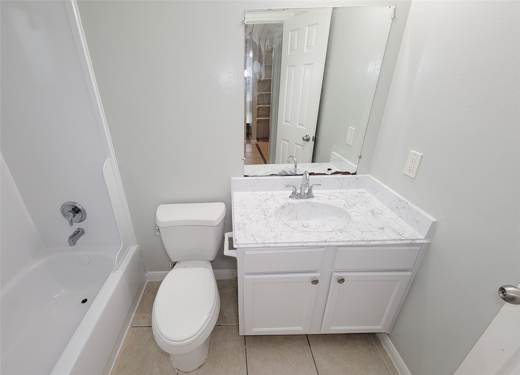 Modern bathroom with a sleek white vanity and marble-style countertop, featuring a spacious mirror and a clean bathtub-shower combo.