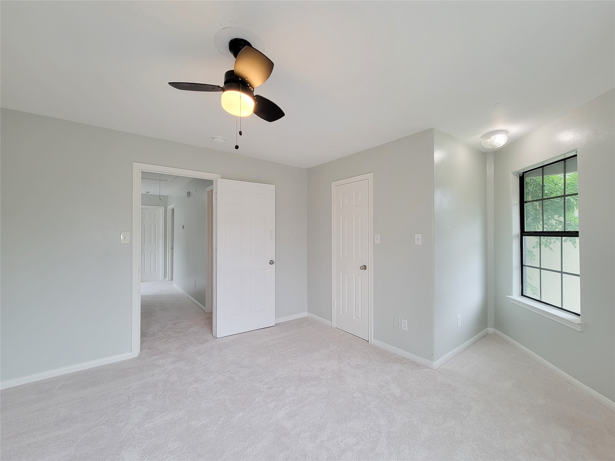 Bright and airy bedroom featuring soft carpeting, neutral walls, a ceiling fan, and a large window that invites natural light.