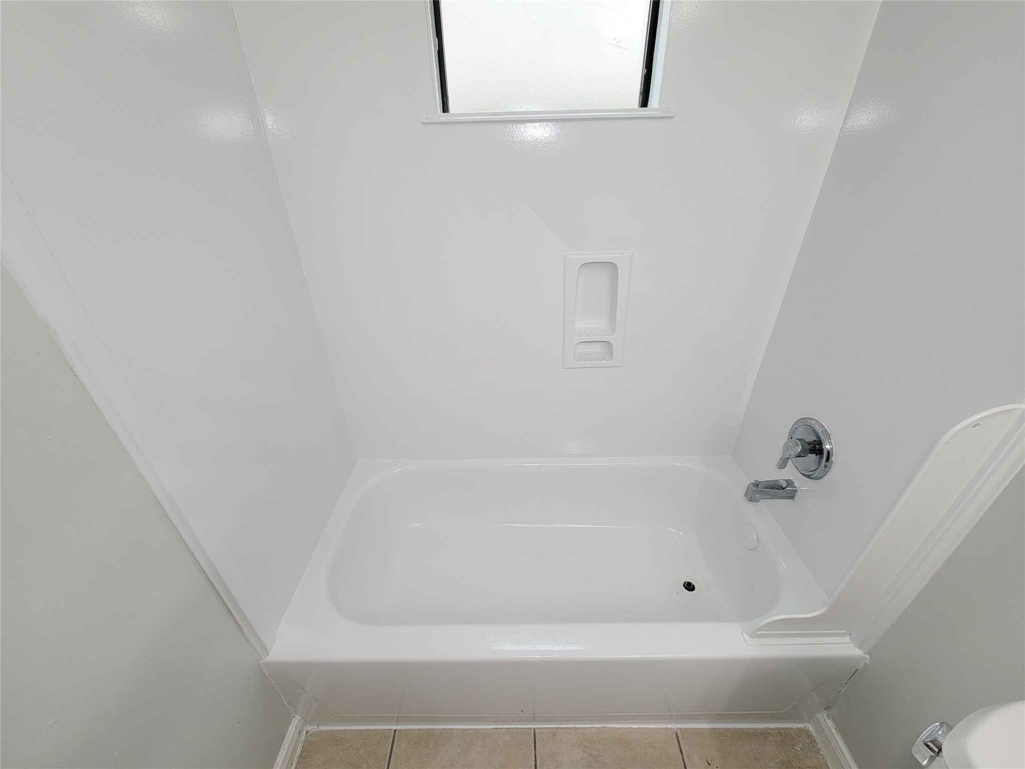 Modern bathroom featuring a pristine white bathtub with sleek fixtures, complemented by neutral tile flooring and a frosted window for privacy.