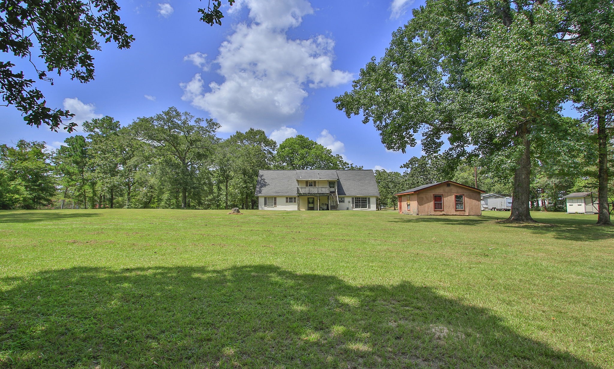 Large, mature trees are scattered throughout the acreage, creating a peaceful country setting with a private well, workshop, chicken coop, and plenty of outdoor storage space.