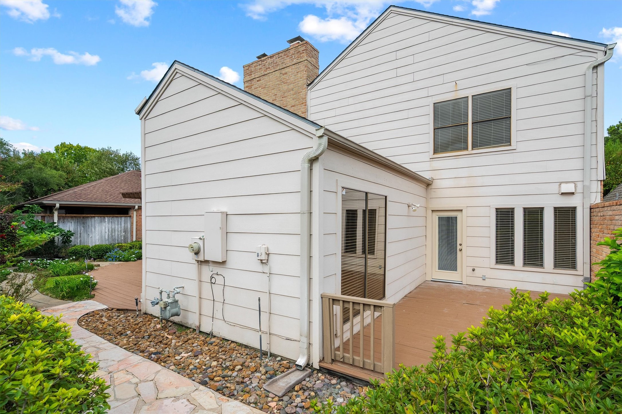 Charming two-story home featuring a spacious wooden deck, perfect for outdoor gatherings, surrounded by lush greenery and a well-maintained garden path.