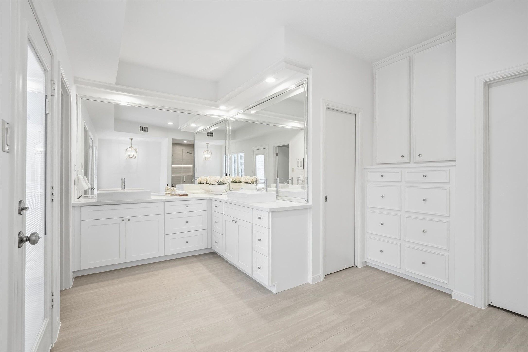 Spacious and elegant bathroom featuring sleek white cabinetry, ample storage, and a large mirror enhancing the bright, airy feel.