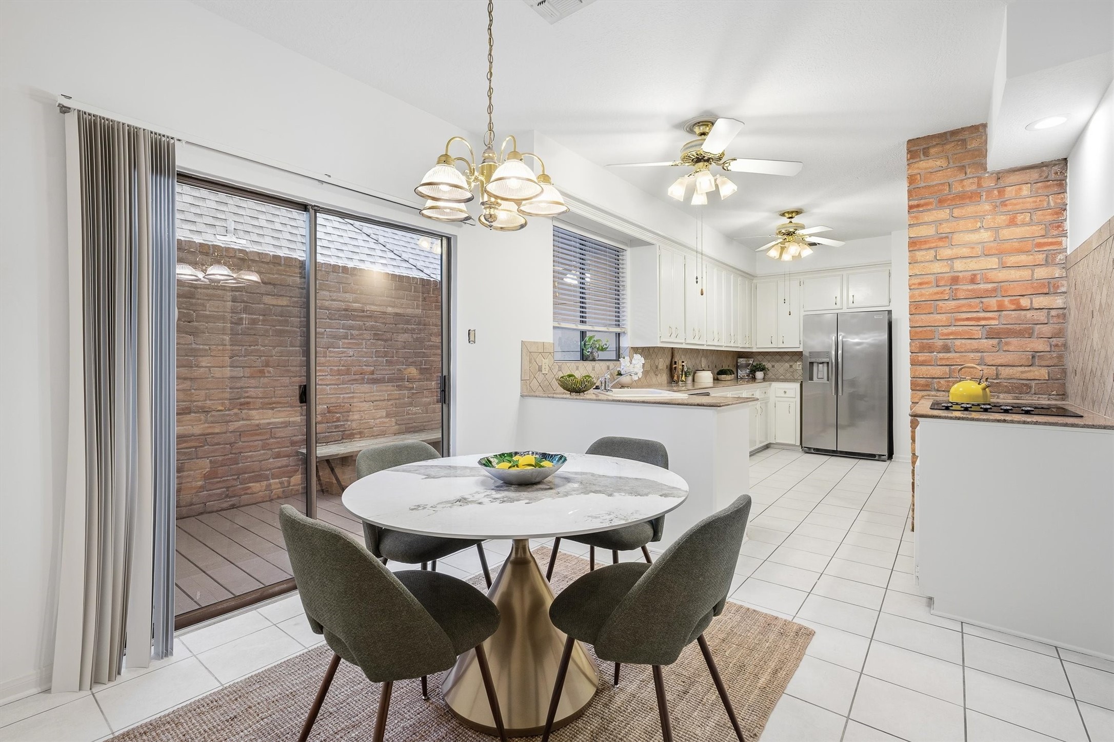 Bright and inviting kitchen-dining area featuring sleek stainless steel appliances, and a charming brick accent wall, all enhanced by ample natural light from large sliding glass doors.