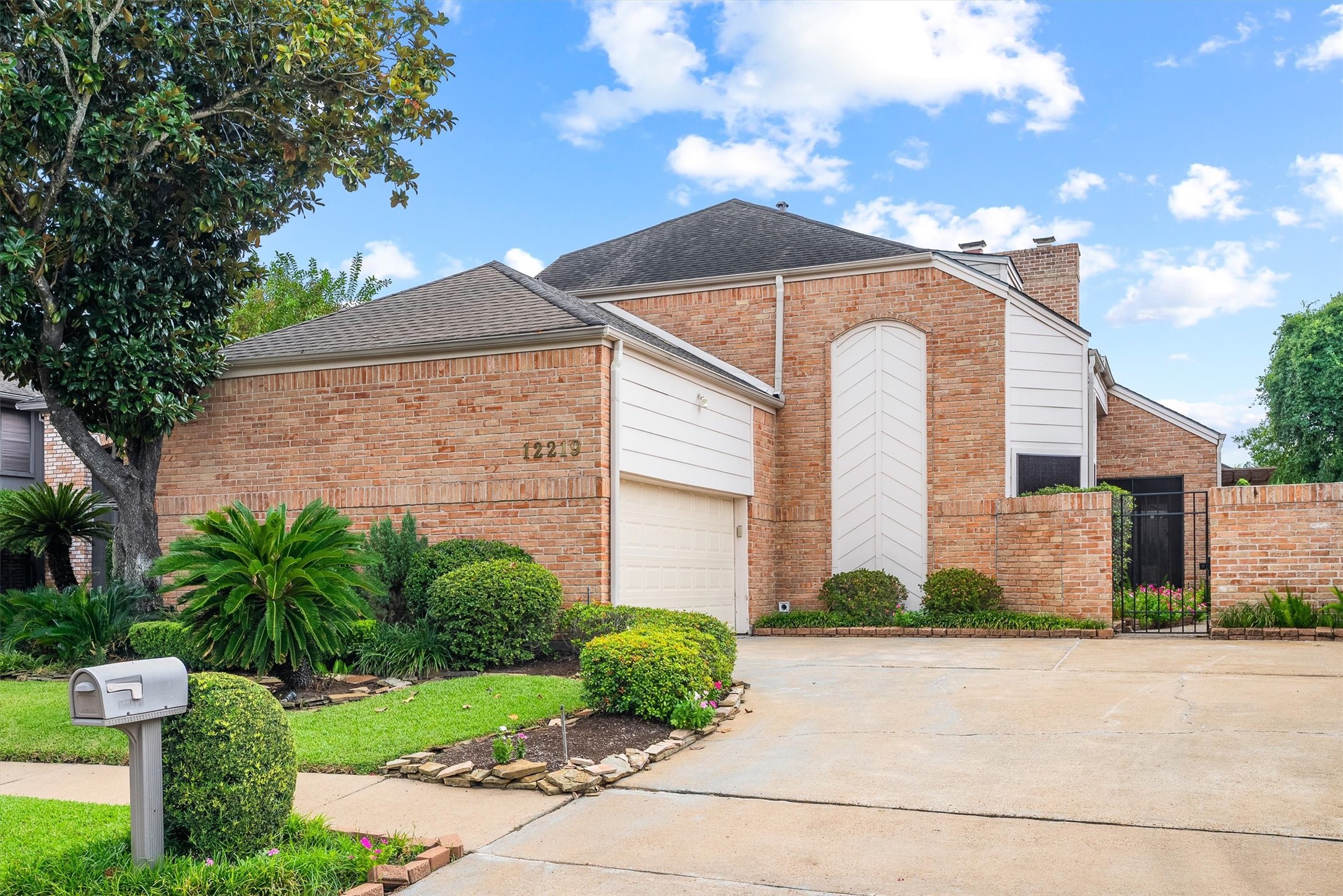 Charming brick home with a welcoming driveway and lush landscaping, offering a blend of privacy and curb appeal.