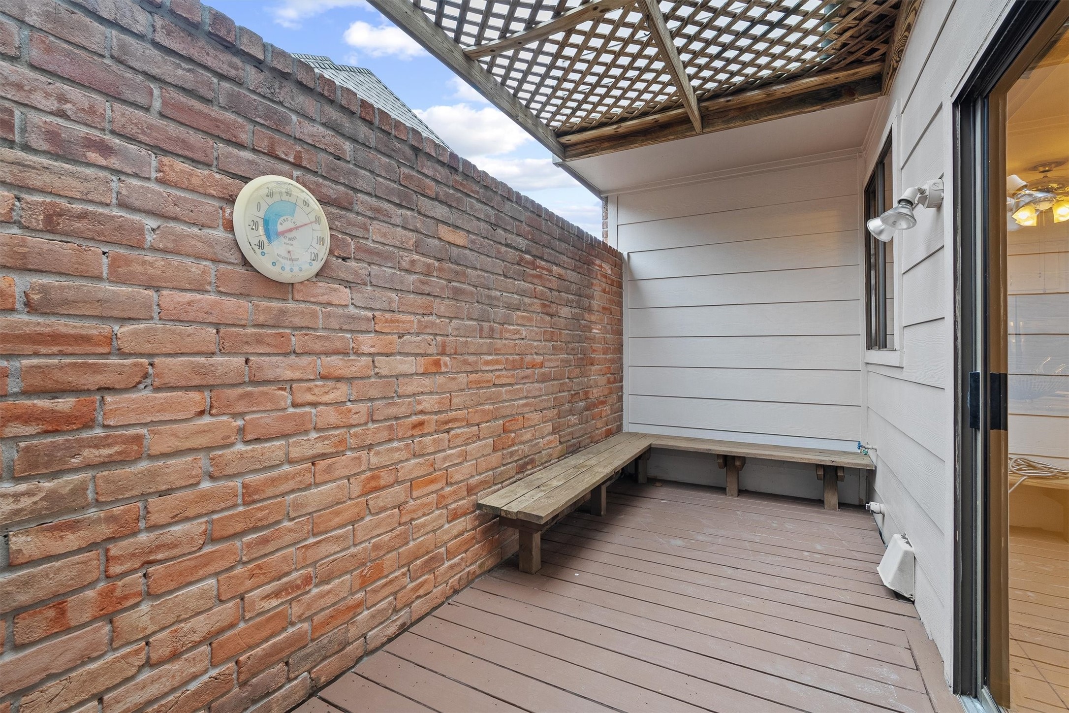 Charming private patio with a rustic brick wall, cozy bench seating, and a lattice roof, perfect for relaxing and enjoying the outdoors.