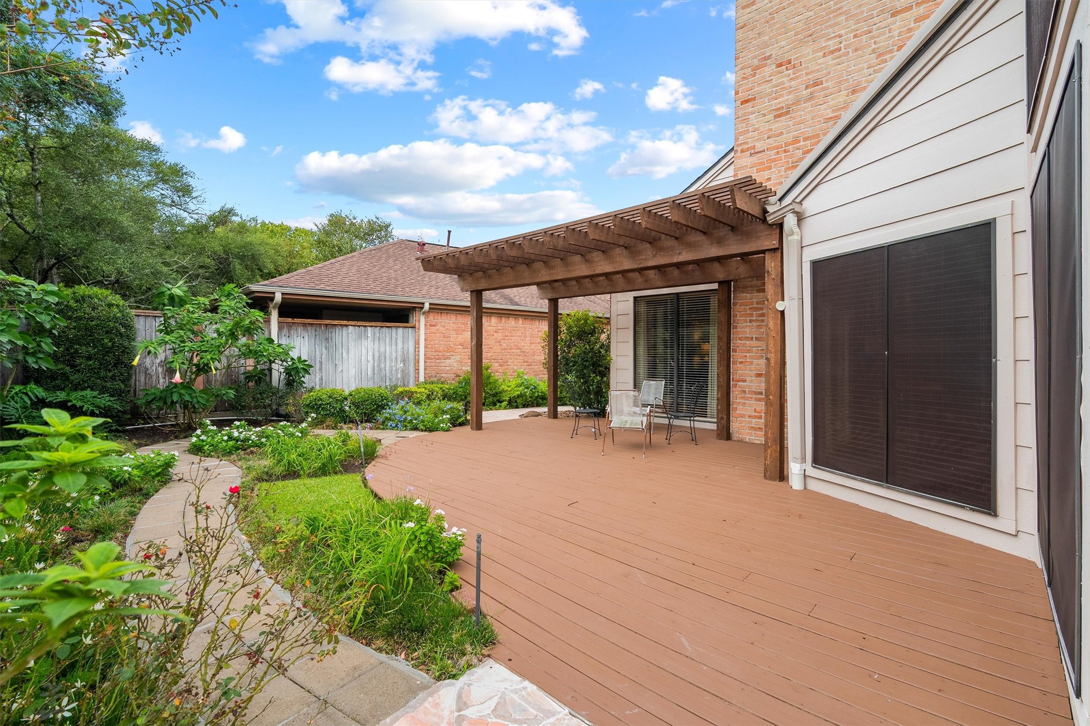 Enjoy a beautifully landscaped backyard featuring a spacious wooden deck, inviting pergola, and charming garden pathways; an ideal outdoor retreat for relaxing or entertaining.