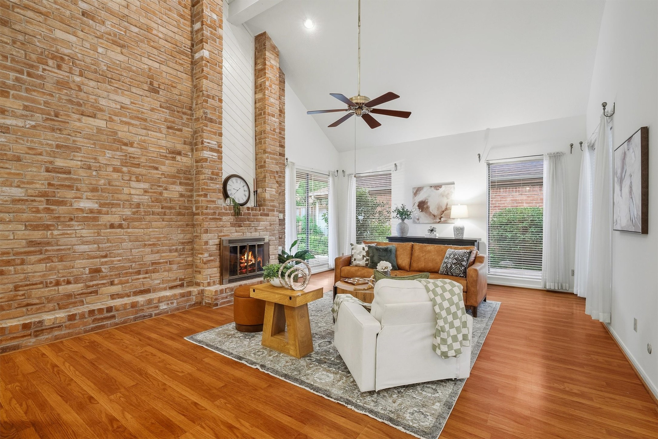 Inviting living room with a stunning brick fireplace, vaulted ceilings, and abundant natural light from large windows, offering a warm and spacious atmosphere.