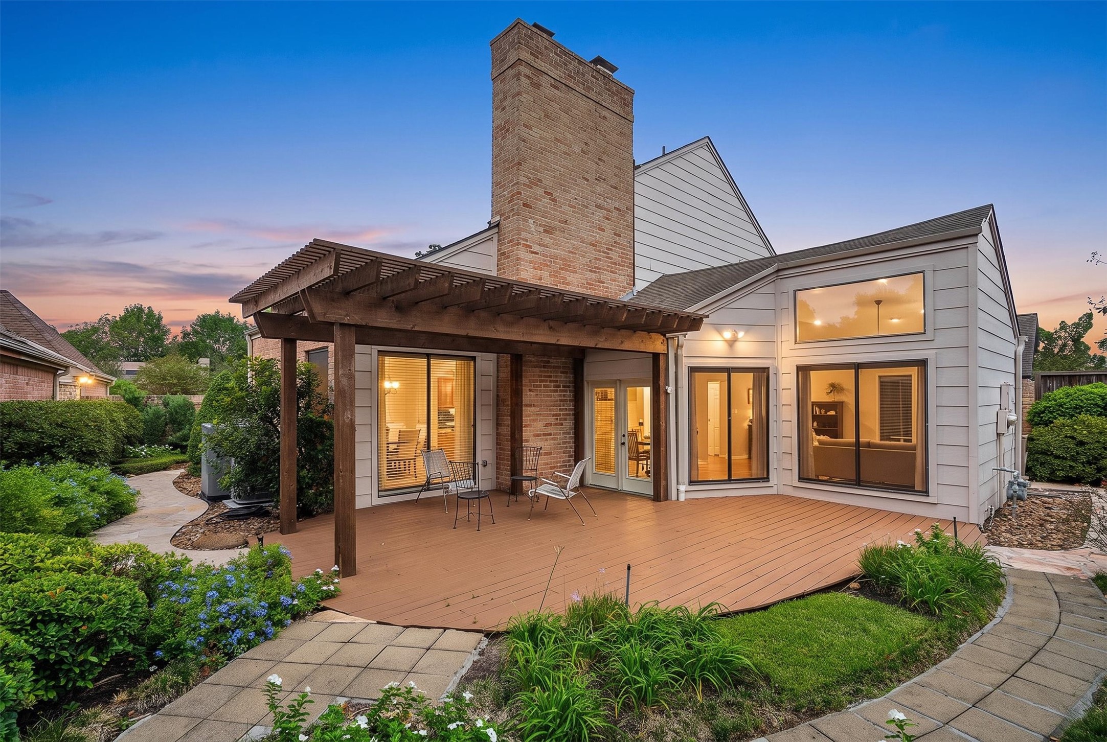 Charming home with a spacious wooden deck and pergola, perfect for outdoor relaxation, surrounded by lush greenery and a beautifully landscaped garden.