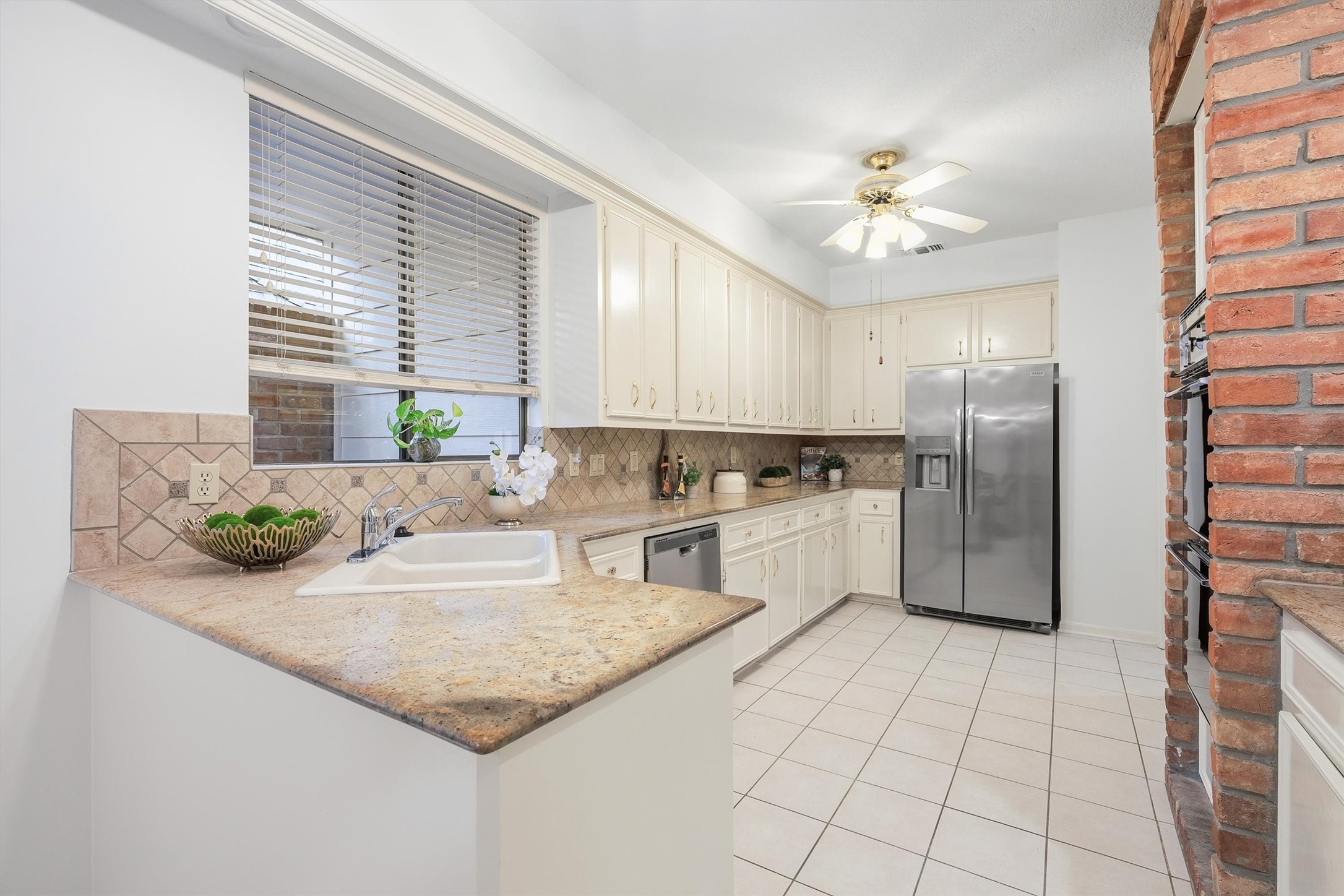 Spacious kitchen with elegant granite countertops, classic white cabinetry, and modern stainless steel appliances, complemented by a charming brick accent wall.