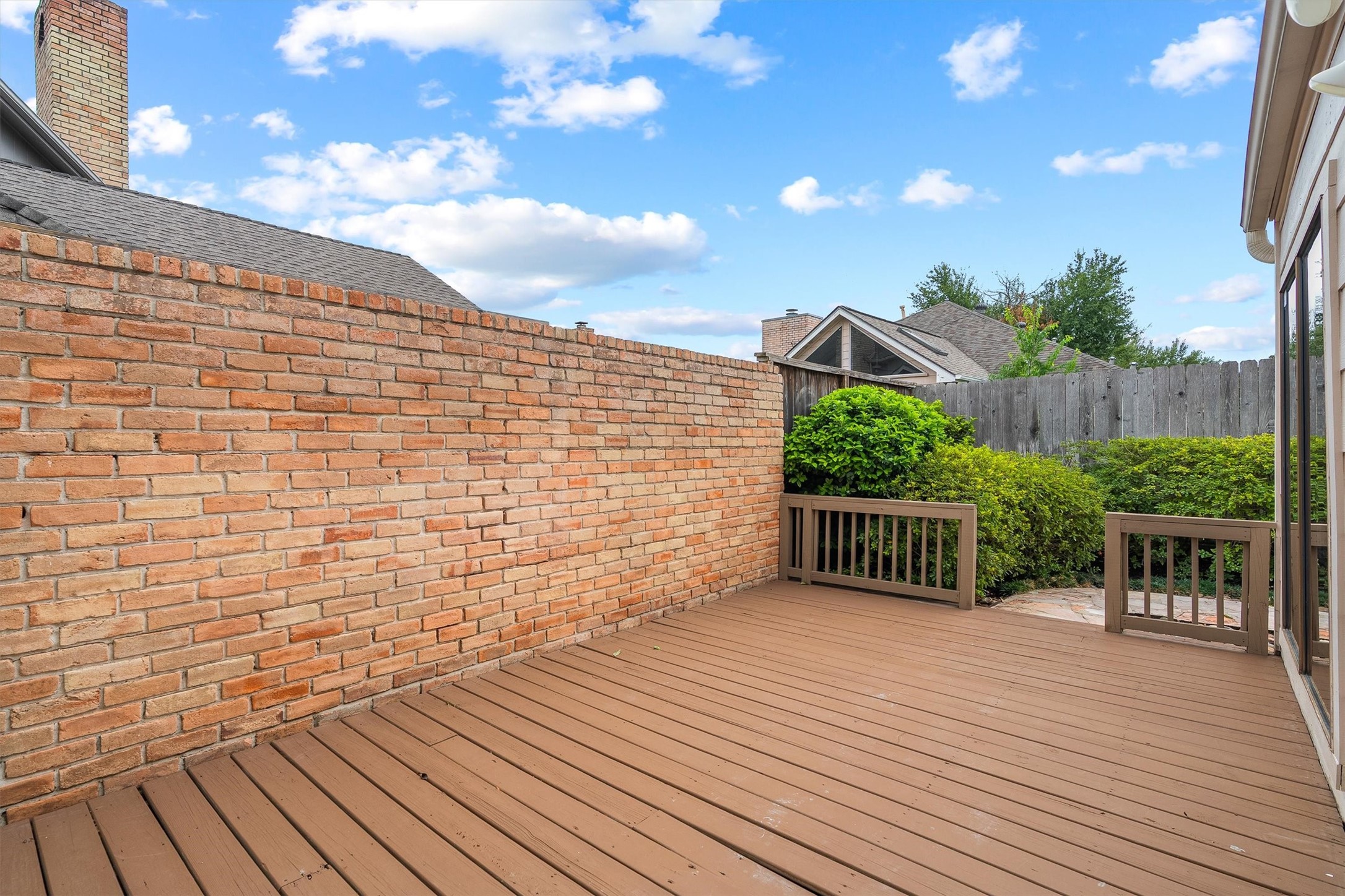 Nice private patio with a wooden deck, surrounded by a brick wall and lush greenery, perfect for outdoor relaxation.