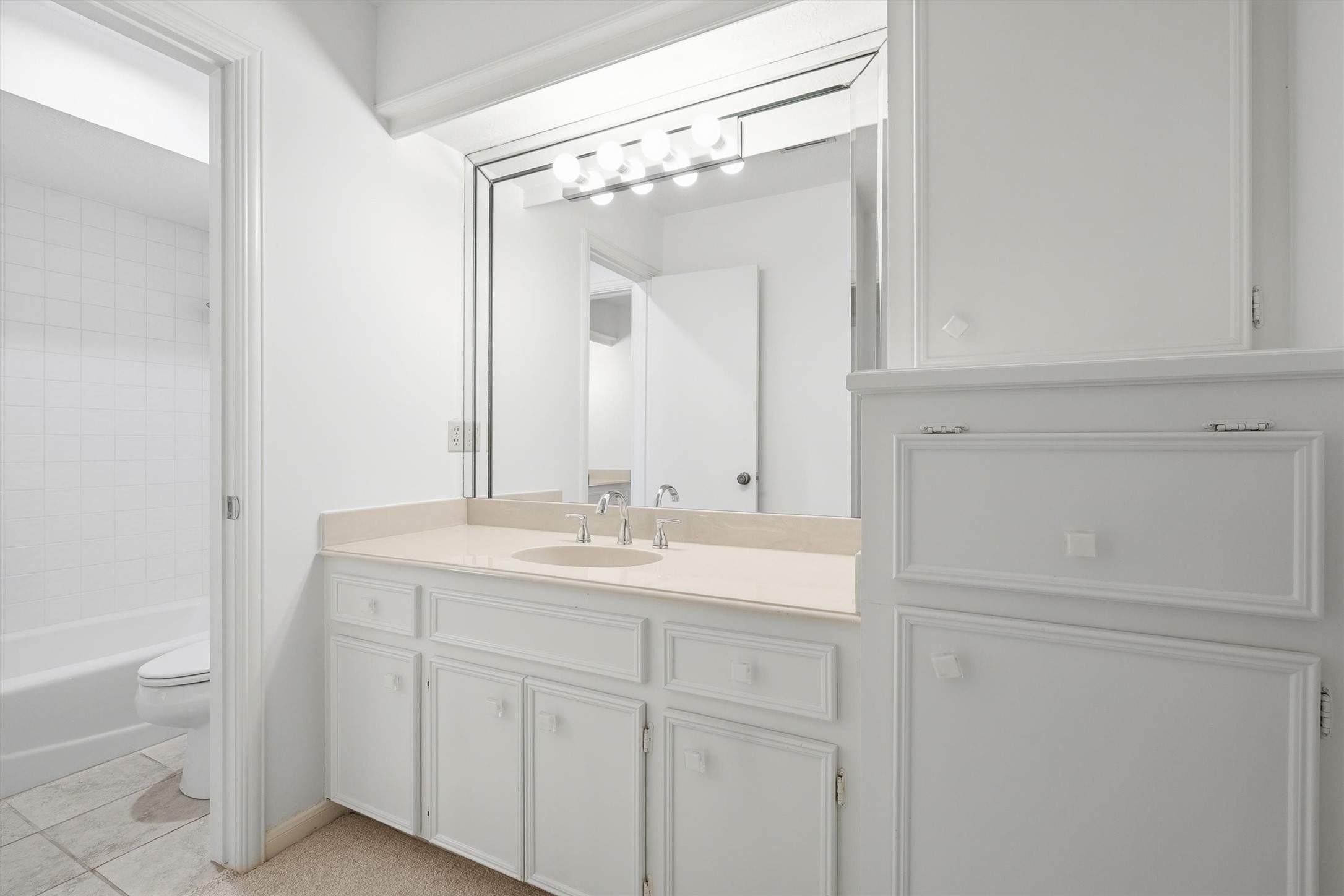 Bright and clean bathroom featuring a spacious vanity with ample storage, a large mirror with modern lighting, and a convenient tub-shower combo.