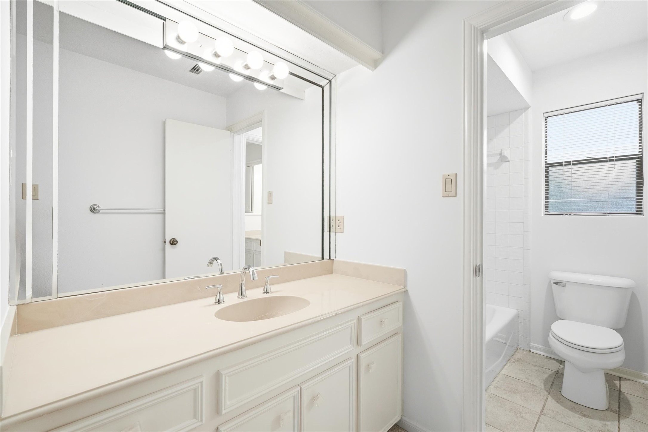 Bright and spacious bathroom featuring a large vanity with ample counter space, modern fixtures, and a sleek mirror, complemented by a tiled shower and natural light from the window.