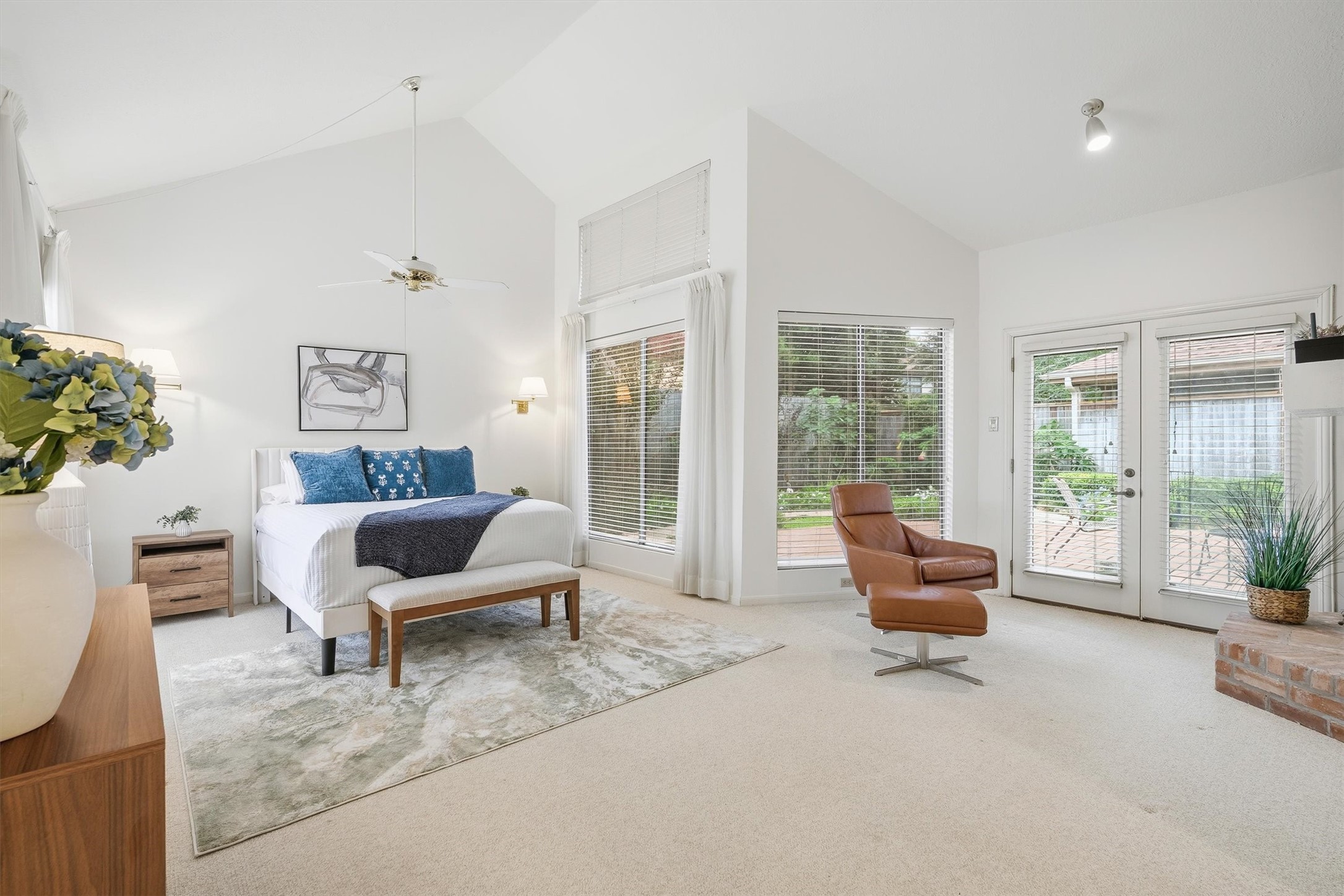 Spacious and bright primary bedroom with high ceilings, featuring large windows and French doors that open to a serene outdoor space.