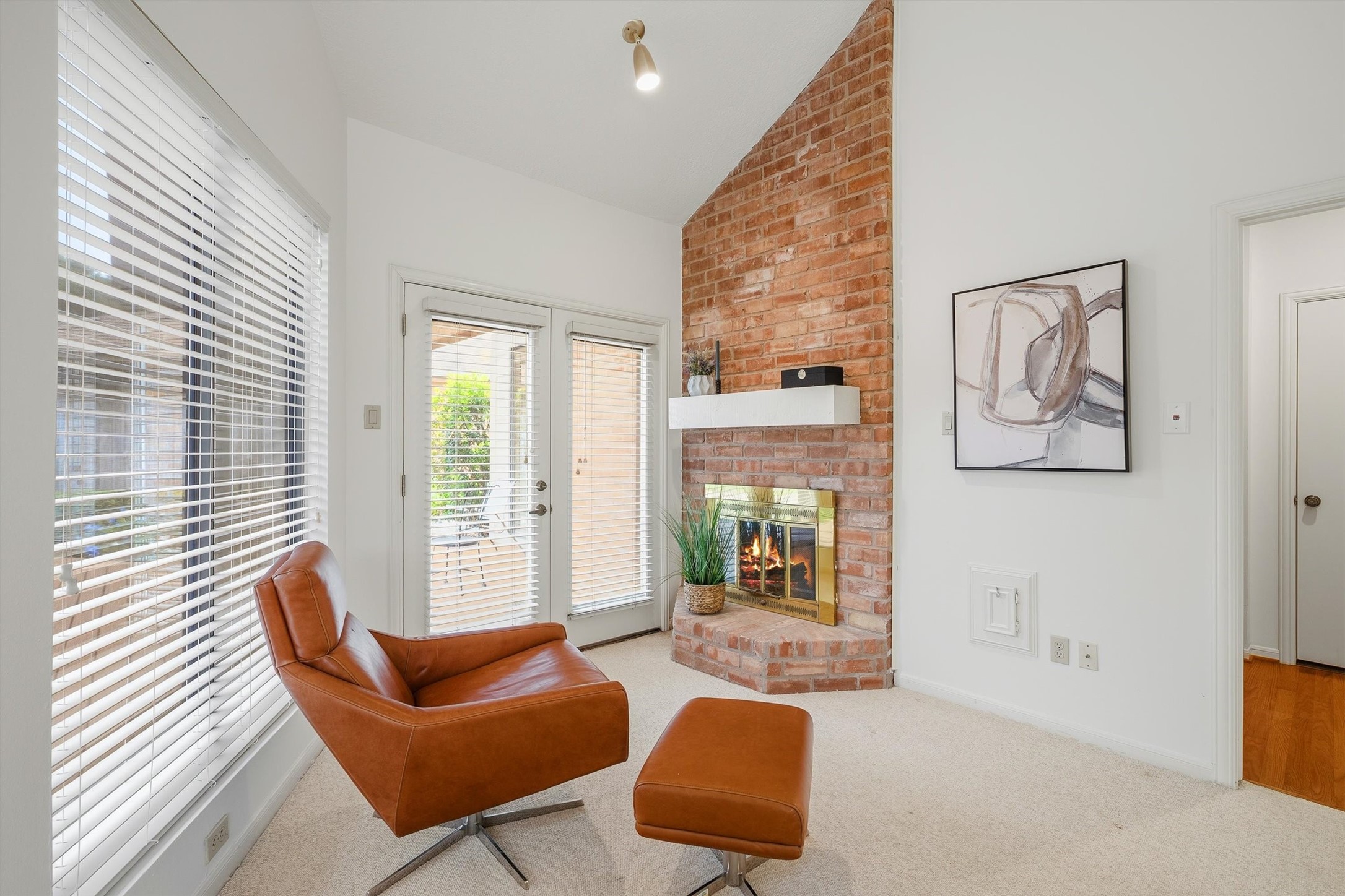 Cozy living space featuring a charming brick fireplace, abundant natural light from large windows and French doors, and a stylish leather chair perfect for relaxation.