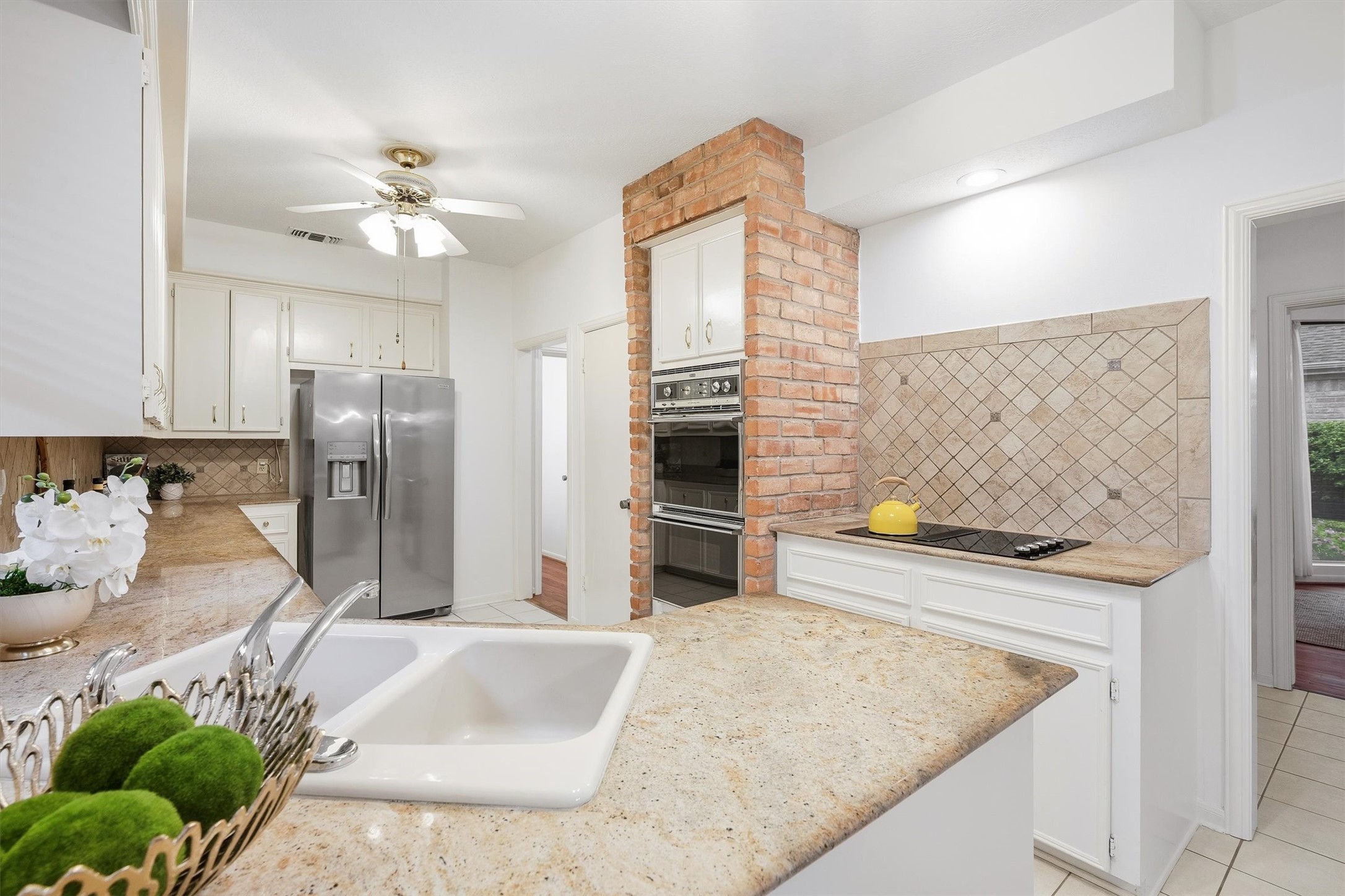 Charming kitchen with a spacious layout featuring modern stainless steel appliances, elegant granite countertops, and a cozy brick accent wall with built-in ovens.