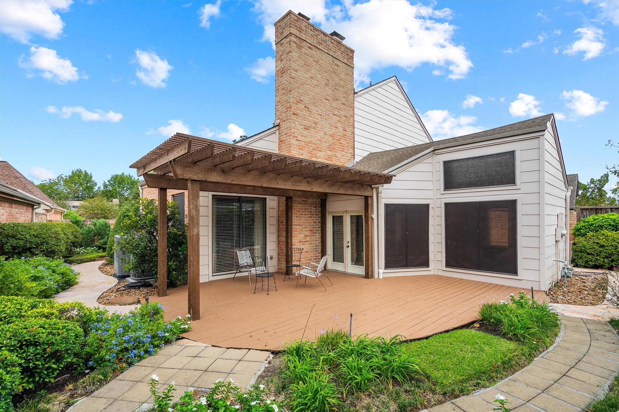 Charming backyard with a spacious wooden deck and pergola, perfect for relaxing or entertaining, surrounded by lush landscaping and garden pathways.
