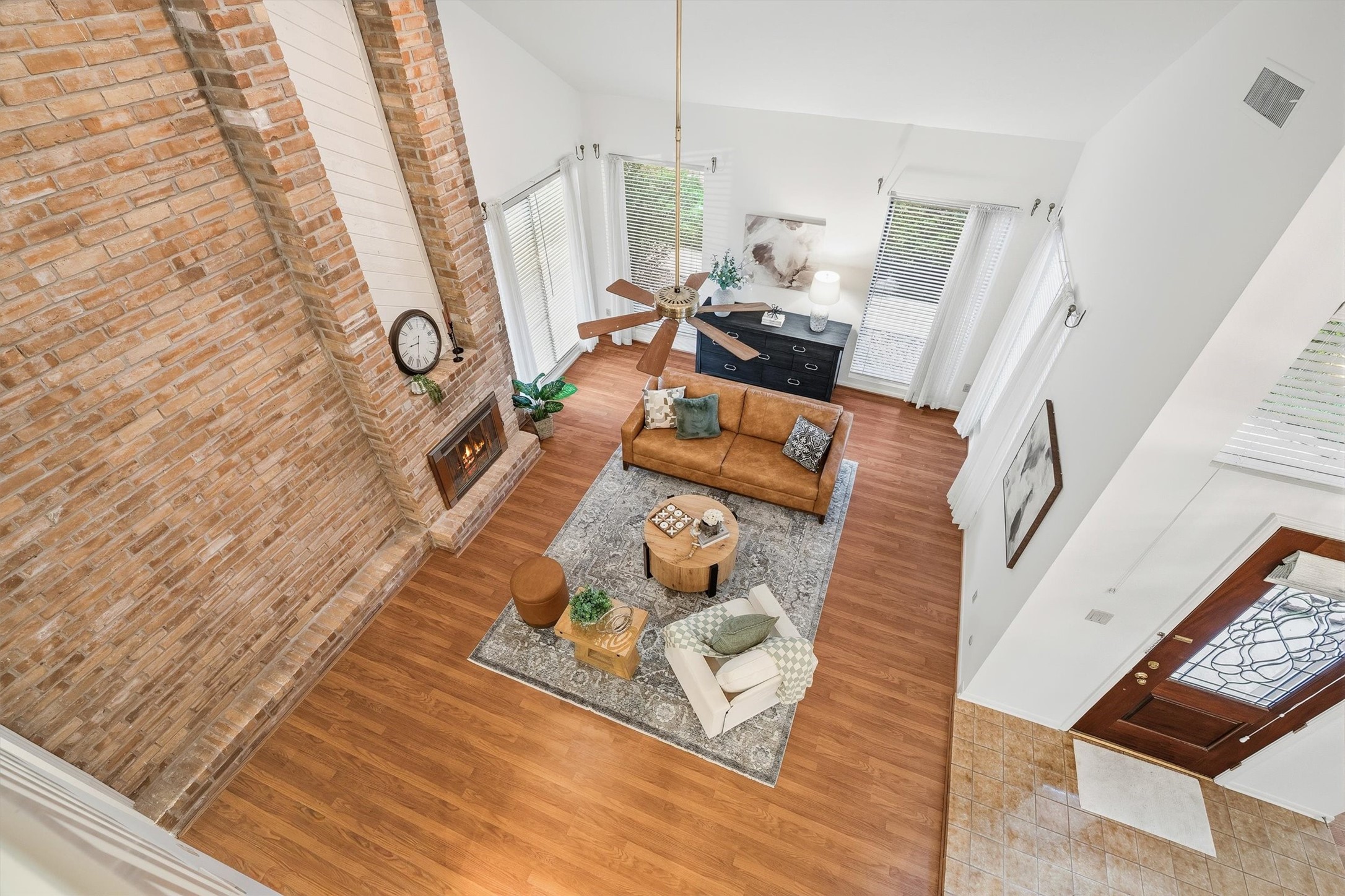 Experience a stunning open-concept living room with soaring ceilings, a striking brick fireplace, and abundant natural light, perfect for relaxation and entertaining.