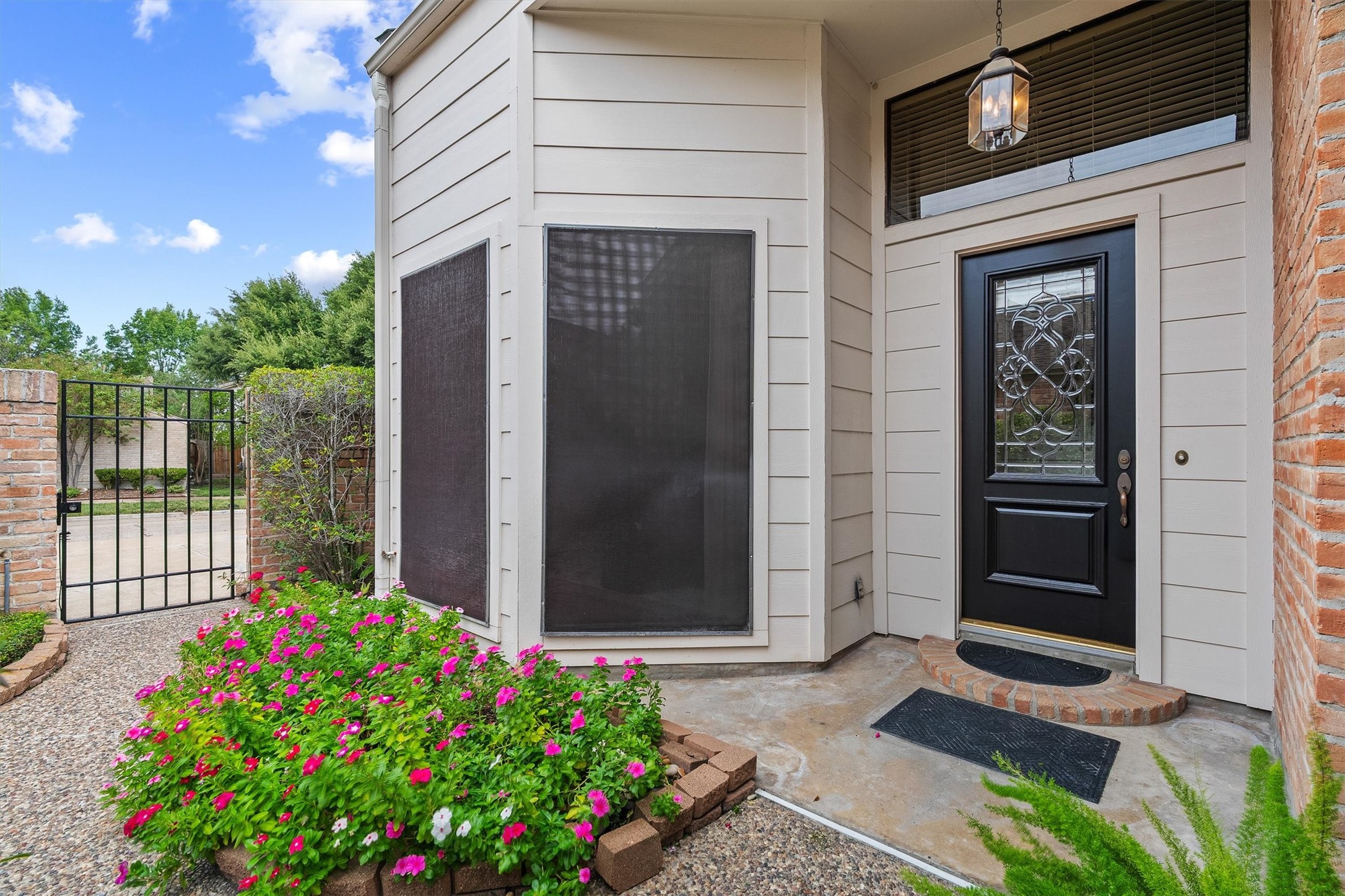 Attractive entrance with elegant black door and intricate glass design, surrounded by lush flowerbeds and a private gated pathway.