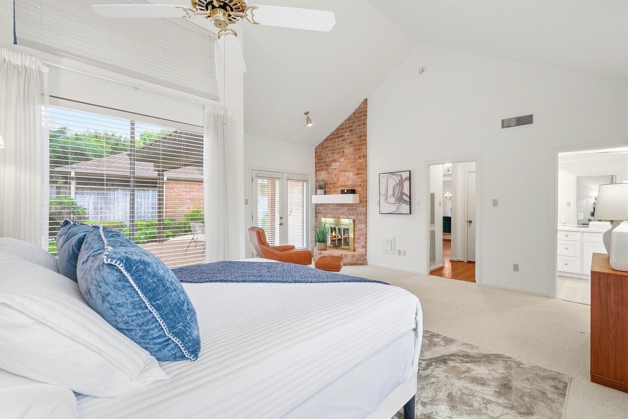 Spacious primary bedroom with a vaulted ceiling, cozy brick fireplace, and large windows offering plenty of natural light.