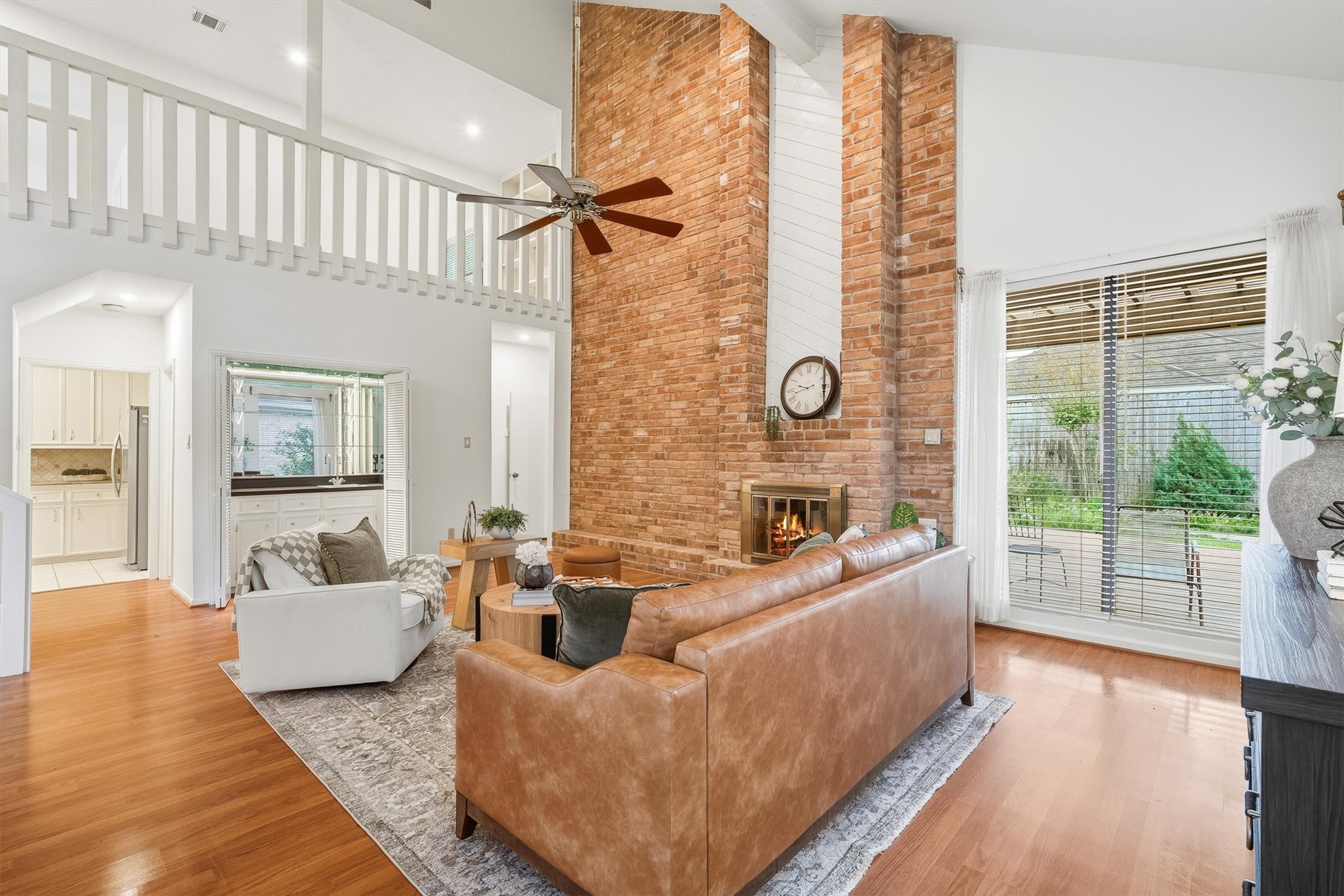 Spacious living area with a striking brick fireplace, high ceilings, and abundant natural light from large windows that overlook a serene backyard.