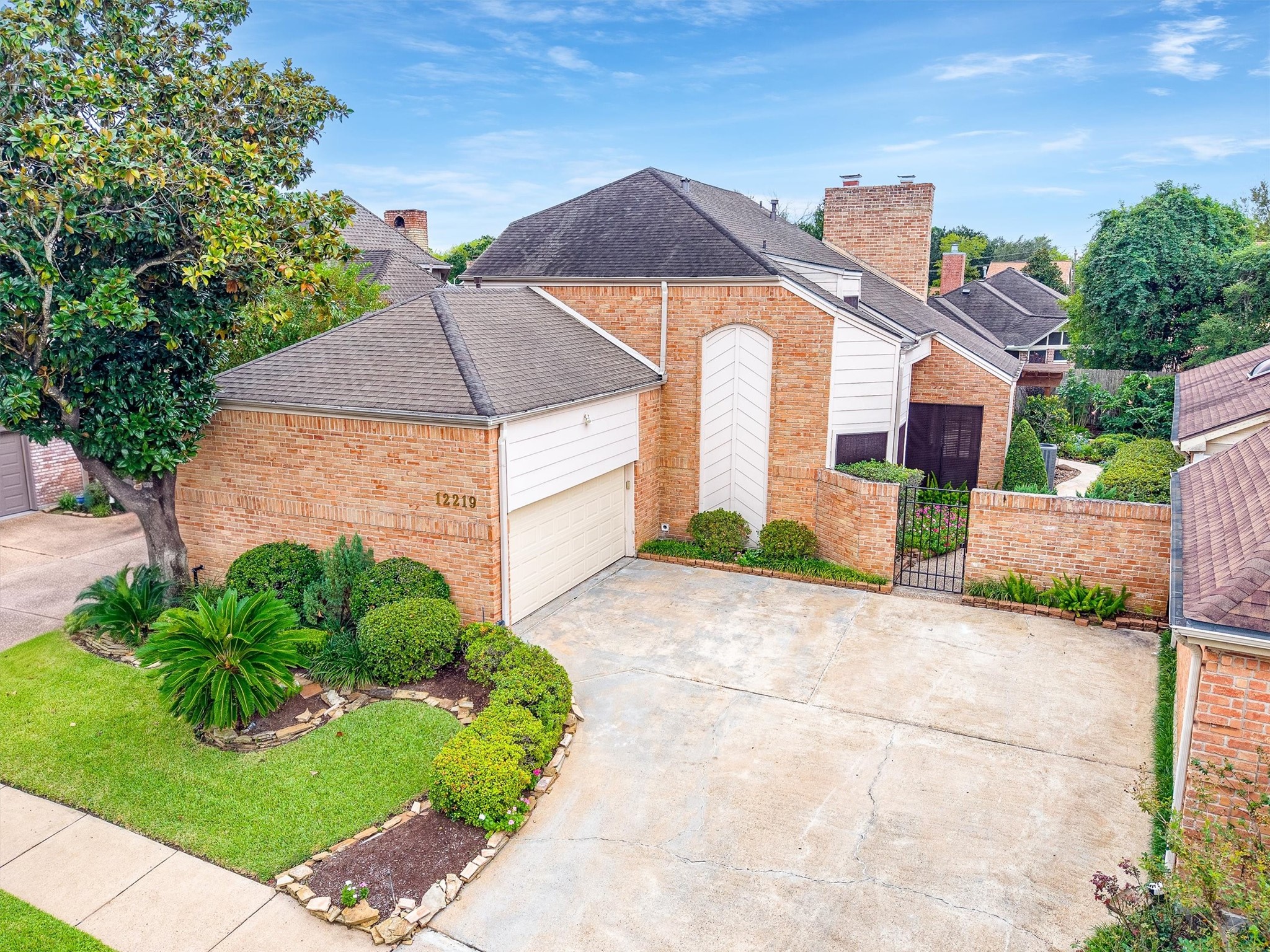 Charming brick home with a two-car garage, lush landscaping, and a gated entrance, offering privacy and curb appeal.
