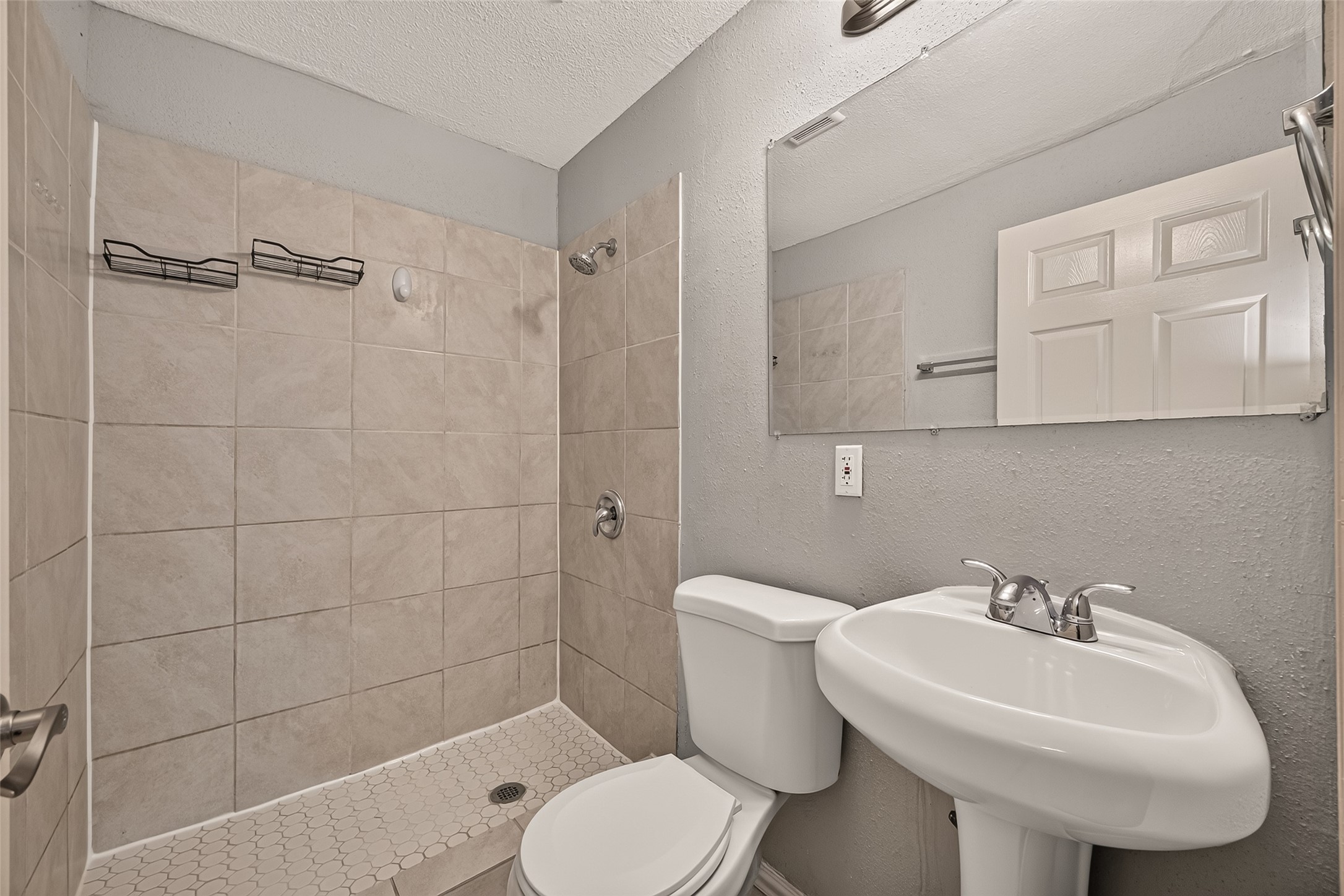 Primary en-suite bath with tiled walk-in shower, tile flooring, and pedestal sink.