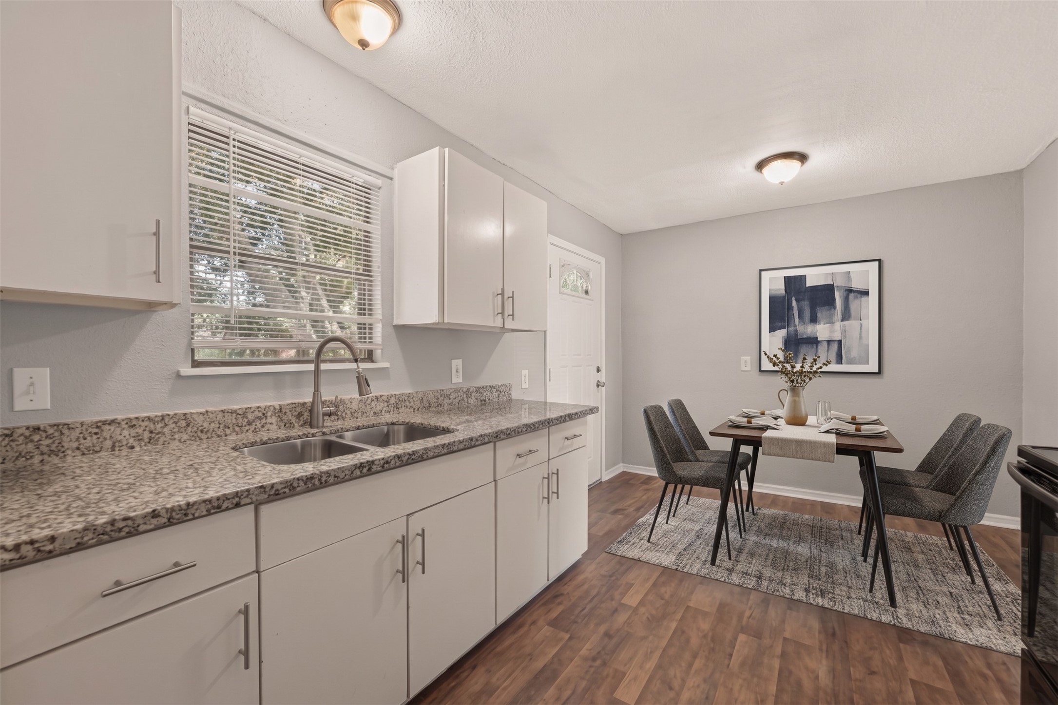 Kitchen with granite countertops, sink under the window, and eat-in dining area. (Virtually staged)
