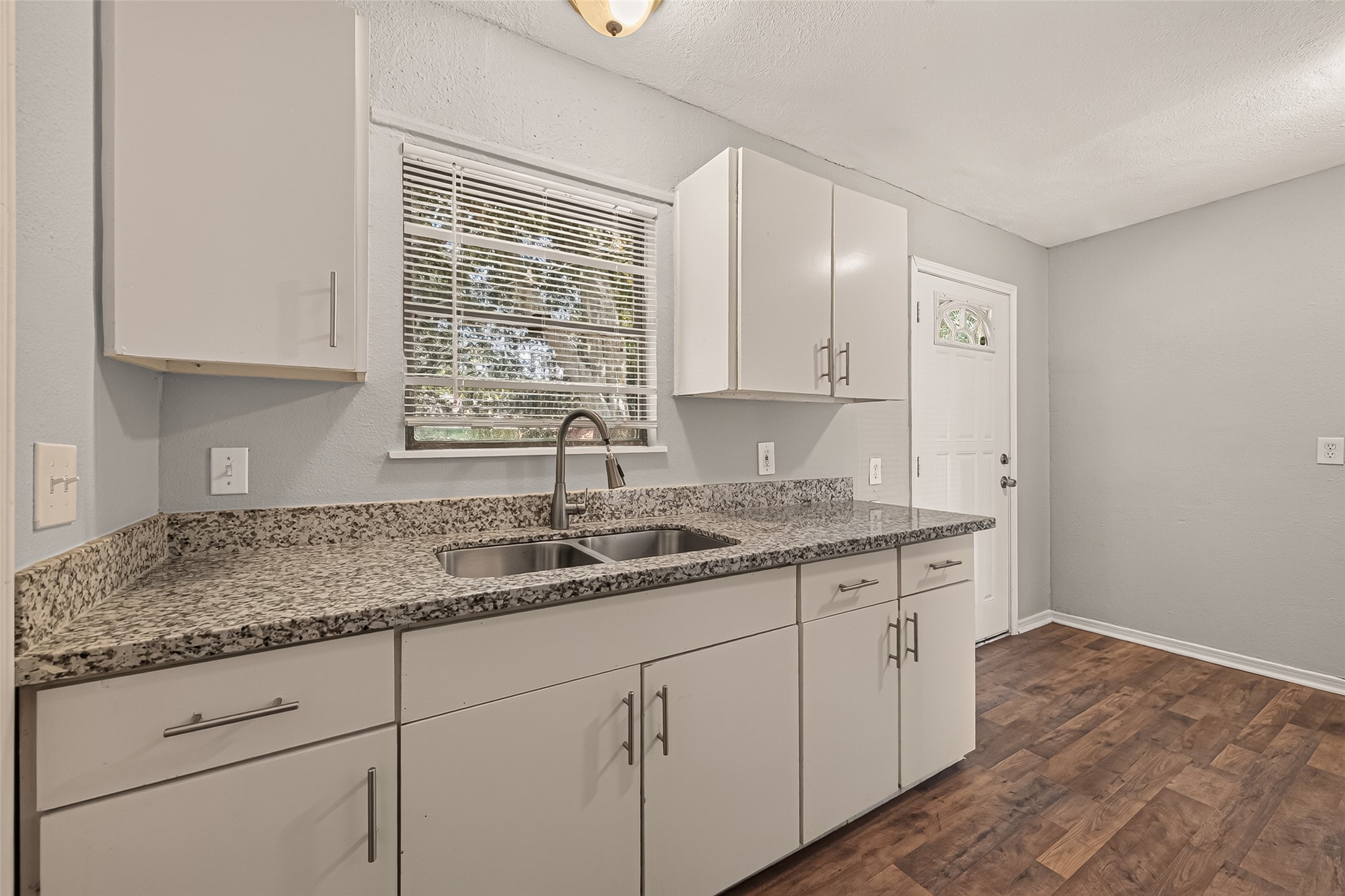 Kitchen sink under the window, with white cabinets and granite countertops.