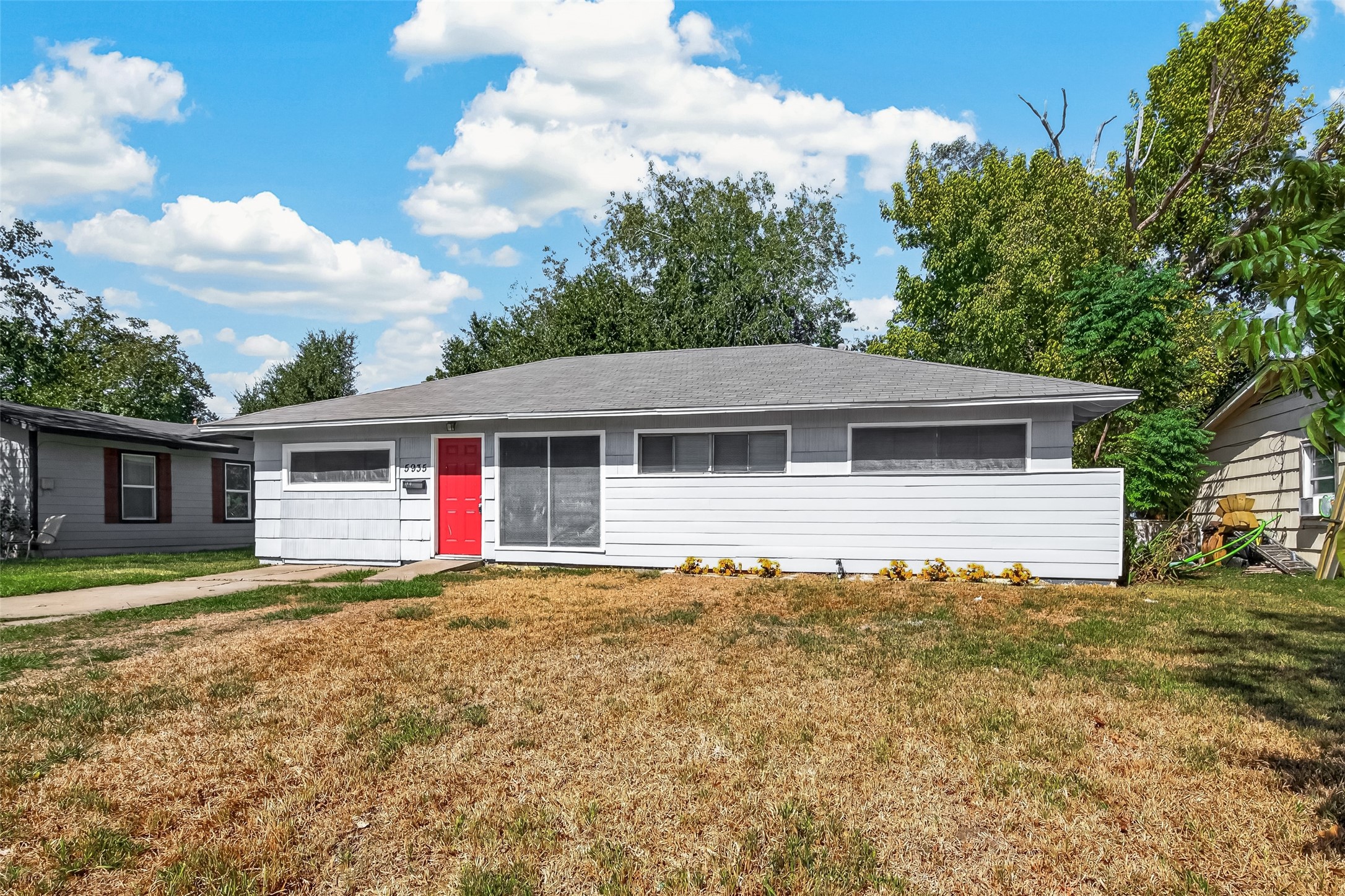 Front exterior: single-story home with red front door and mature trees.