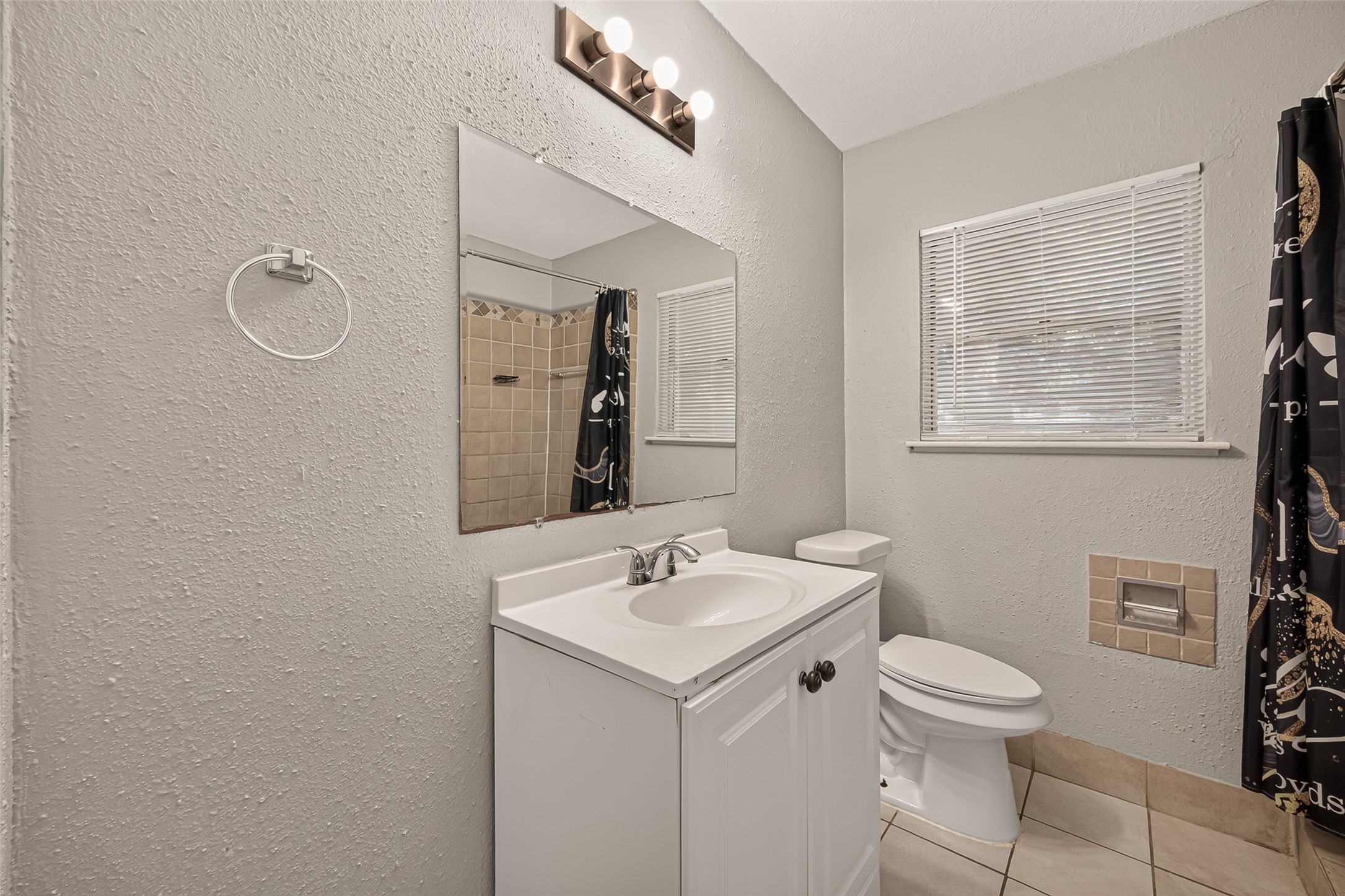 Hall bath with white vanity, tile flooring, and window.