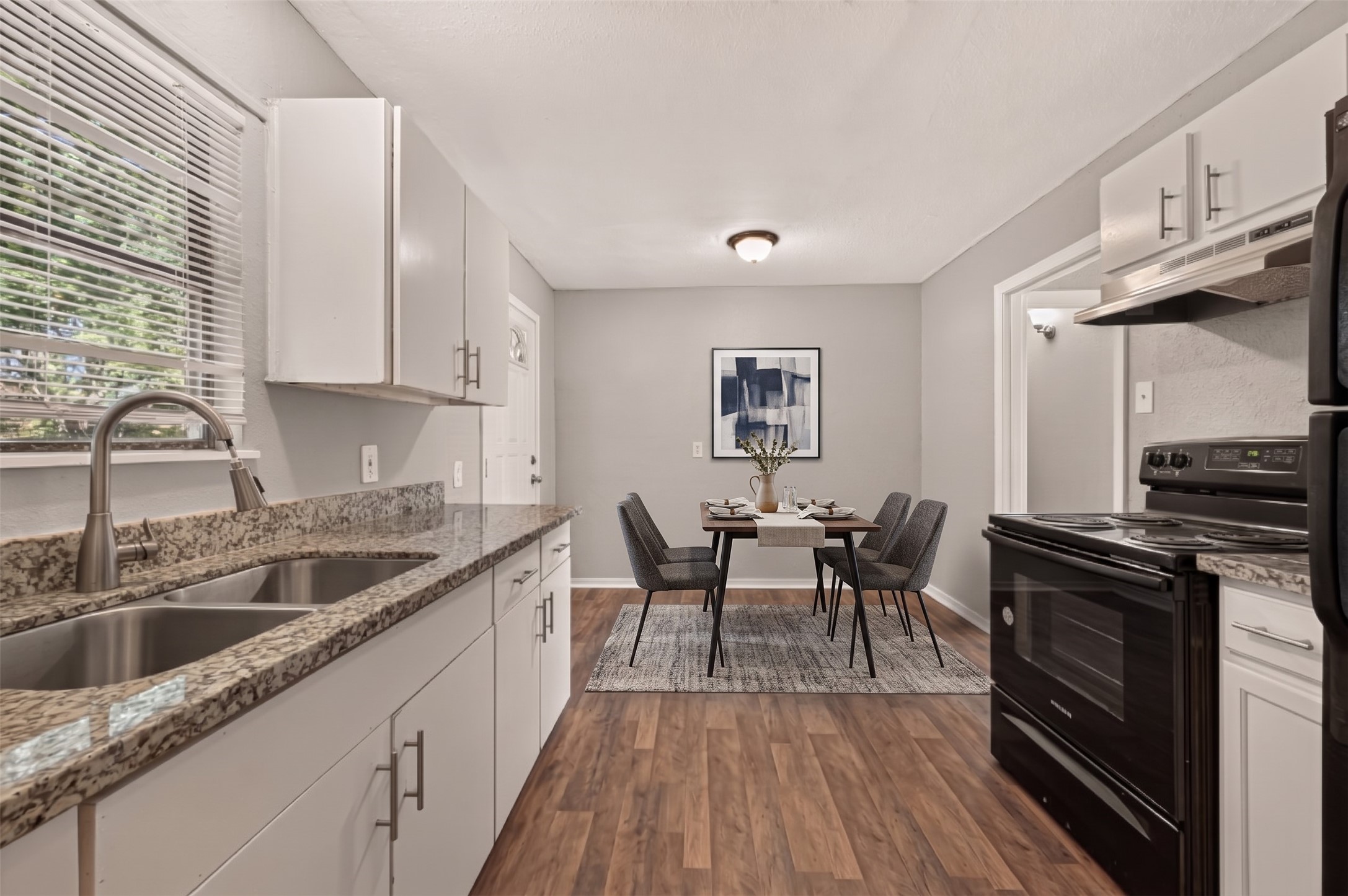 Kitchen with white cabinets, granite countertops, and black range, open to the eat-in dining area. (Virtually staged)