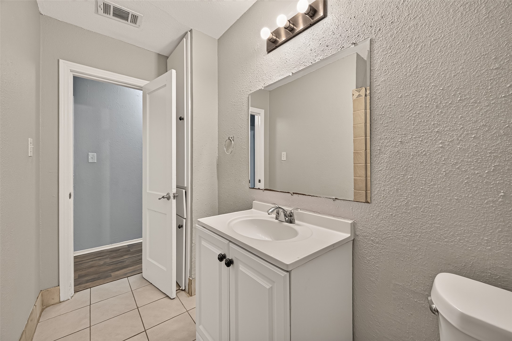 Hall bath with white vanity, tile flooring, and vanity lighting.