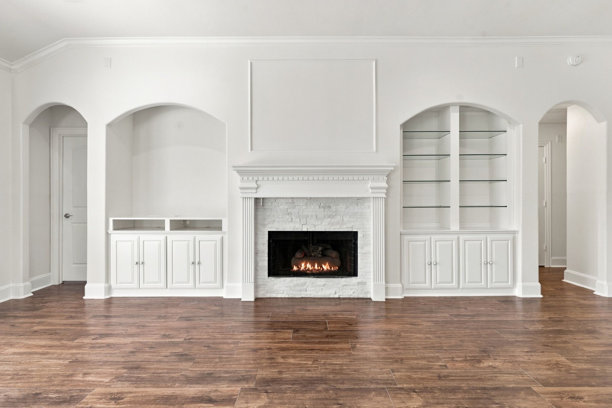 A closer look at the gas-log Fireplace showcases the beautiful mantel with detailed dental molding and the perfect space above for a large-screen TV. Built-in shelving on each side provides an ideal place to display your favorite dcor and treasured pieces, with an additional option for a TV on the left side of the fireplace. The door to the left leads to the private Primary Suite, while the archway to the right leads to the Secondary Bedrooms and Full Bath.