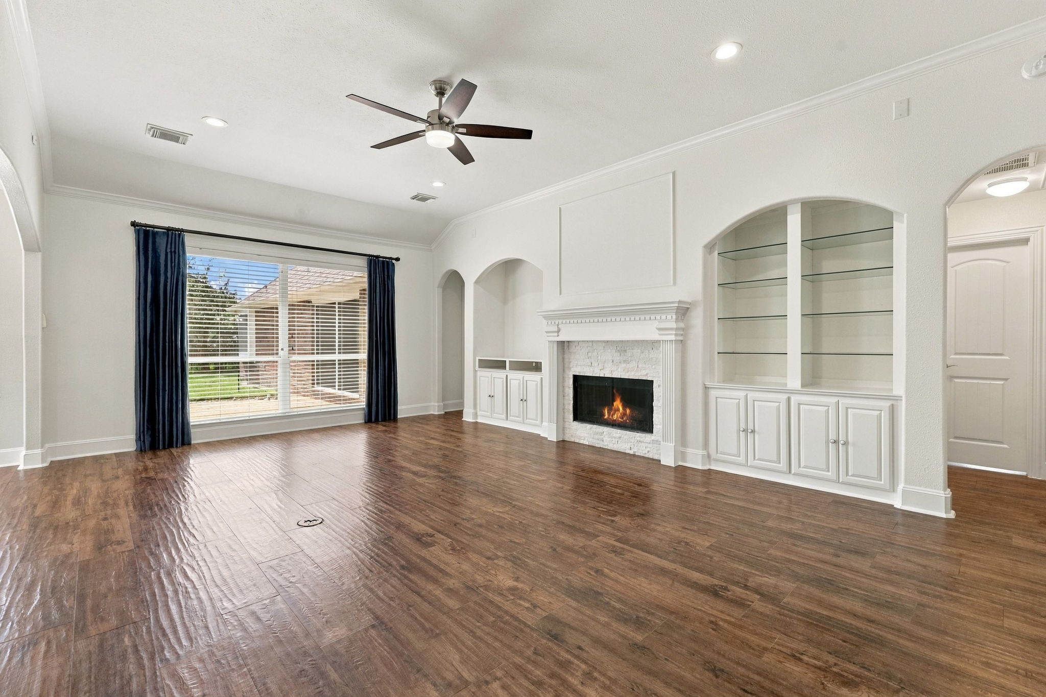 The Family Room is gorgeous and inviting, featuring 10-foot ceilings, elegant crown molding, 5-inch baseboards, and beautiful wood-look tile flooring. Expansive windows with custom drapes fill the room with natural light, while a gas-log fireplace surrounded by stacked stone creates a warm focal point. Convenient built-ins on either side of the fireplace provide the perfect combination of style and functionality.