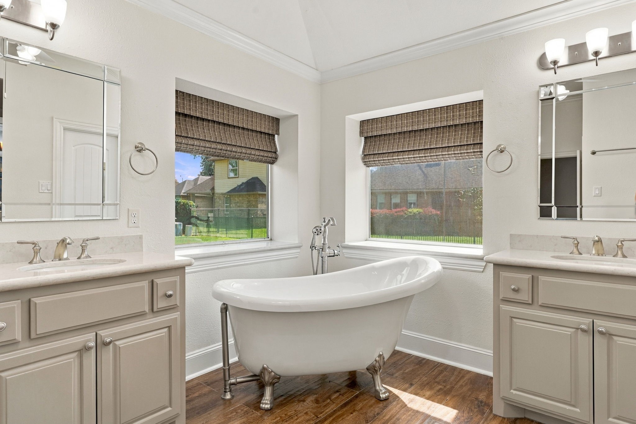 The freestanding soaking tub is beautifully positioned in the corner and features a brushed nickel faucet with a separate handheld wand. Framed by two windows with elegant Roman shades, this serene space creates the perfect setting to relax and unwind.