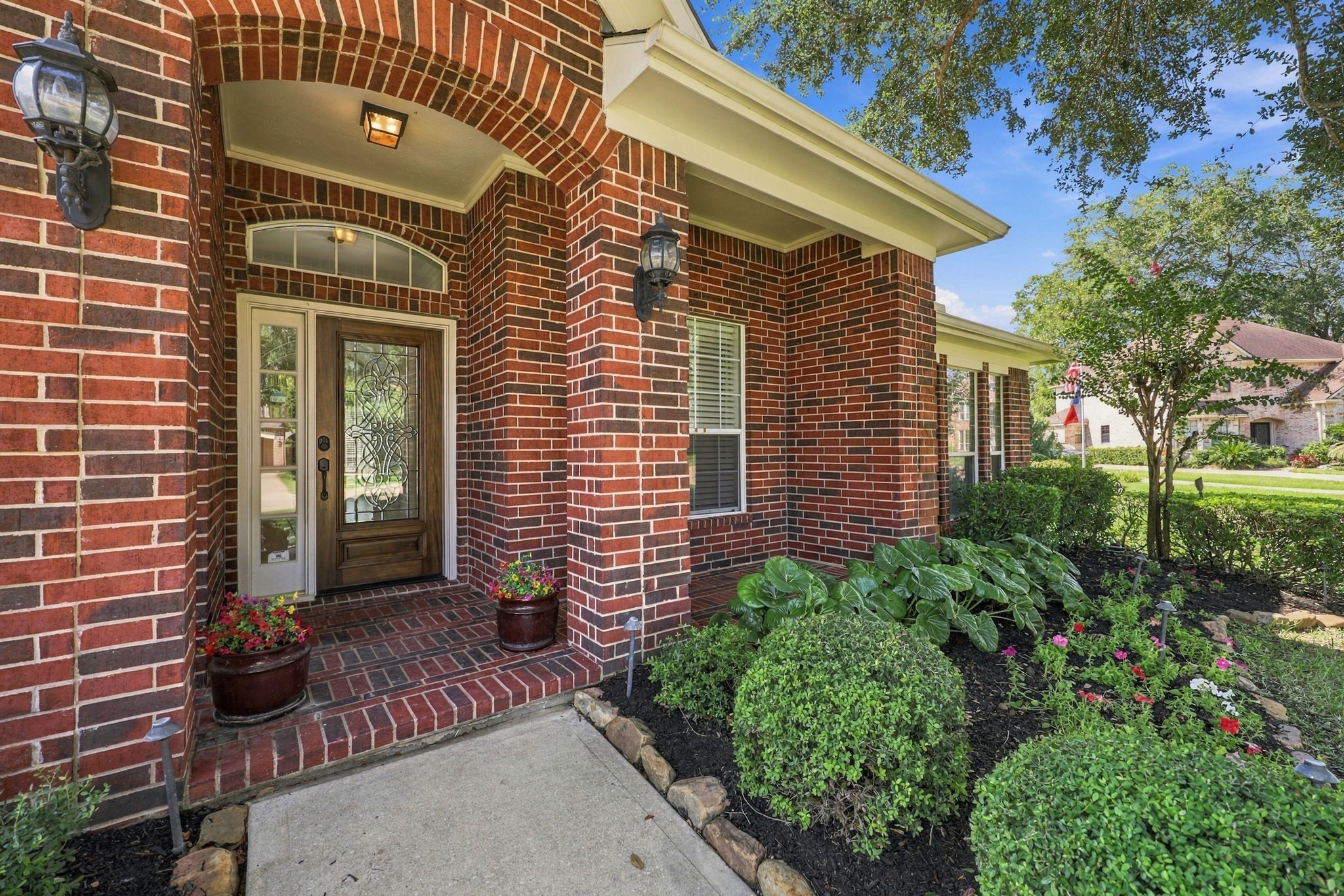 The covered Front Porch offers an inviting welcome with beautiful brick flooring, elegant black coach lights, and a gorgeous leaded-glass wood front door that adds timeless charm and character to the home.